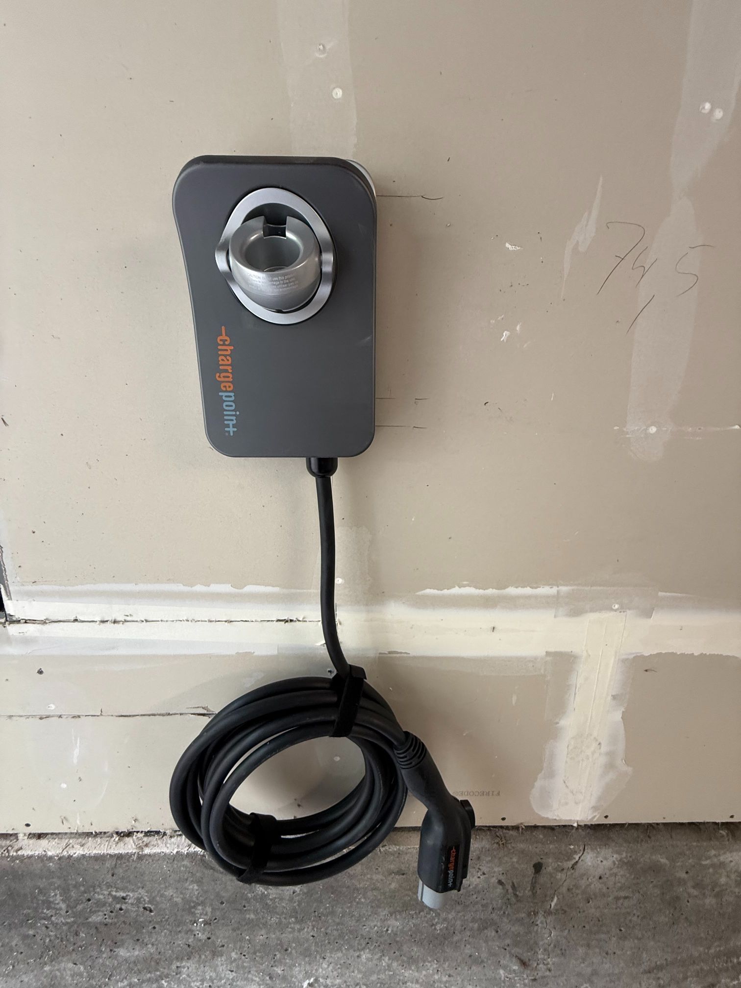 Wall-mounted black device with a silver dial and coiled cord on a beige wall.