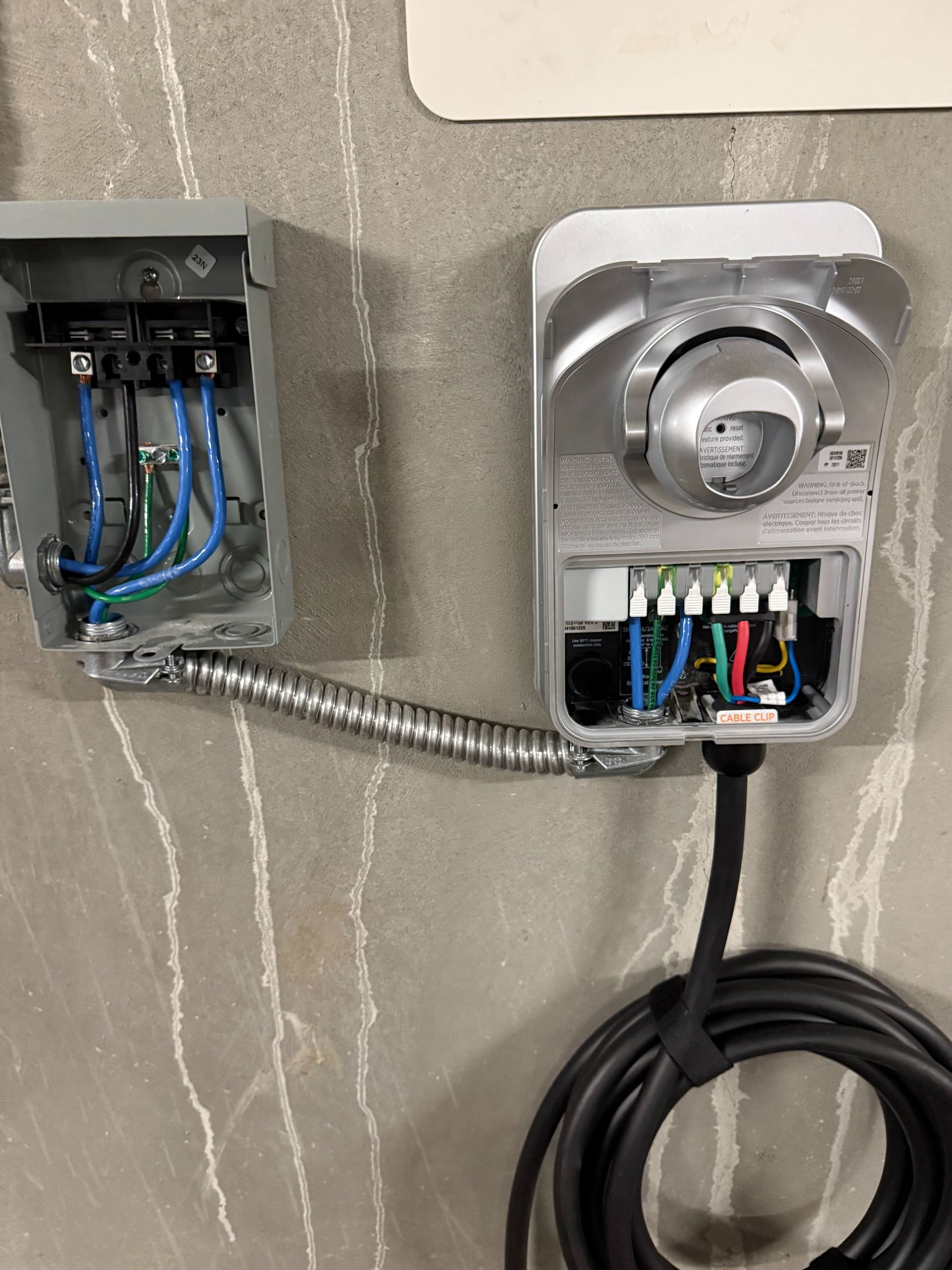 Electrical boxes and conduit on a concrete wall, with a coiled black cable hanging below.