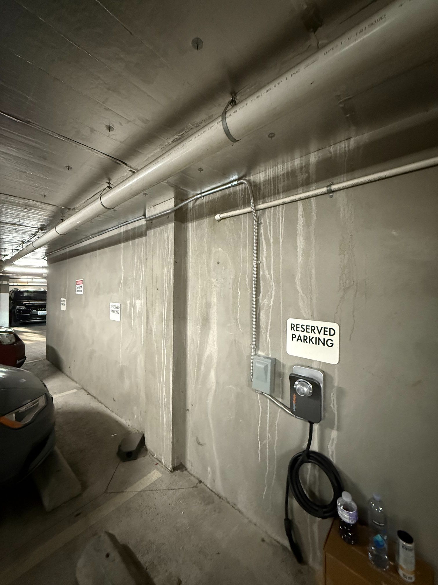 Narrow parking garage corridor with concrete walls, exposed pipes, and a parked car on the left.