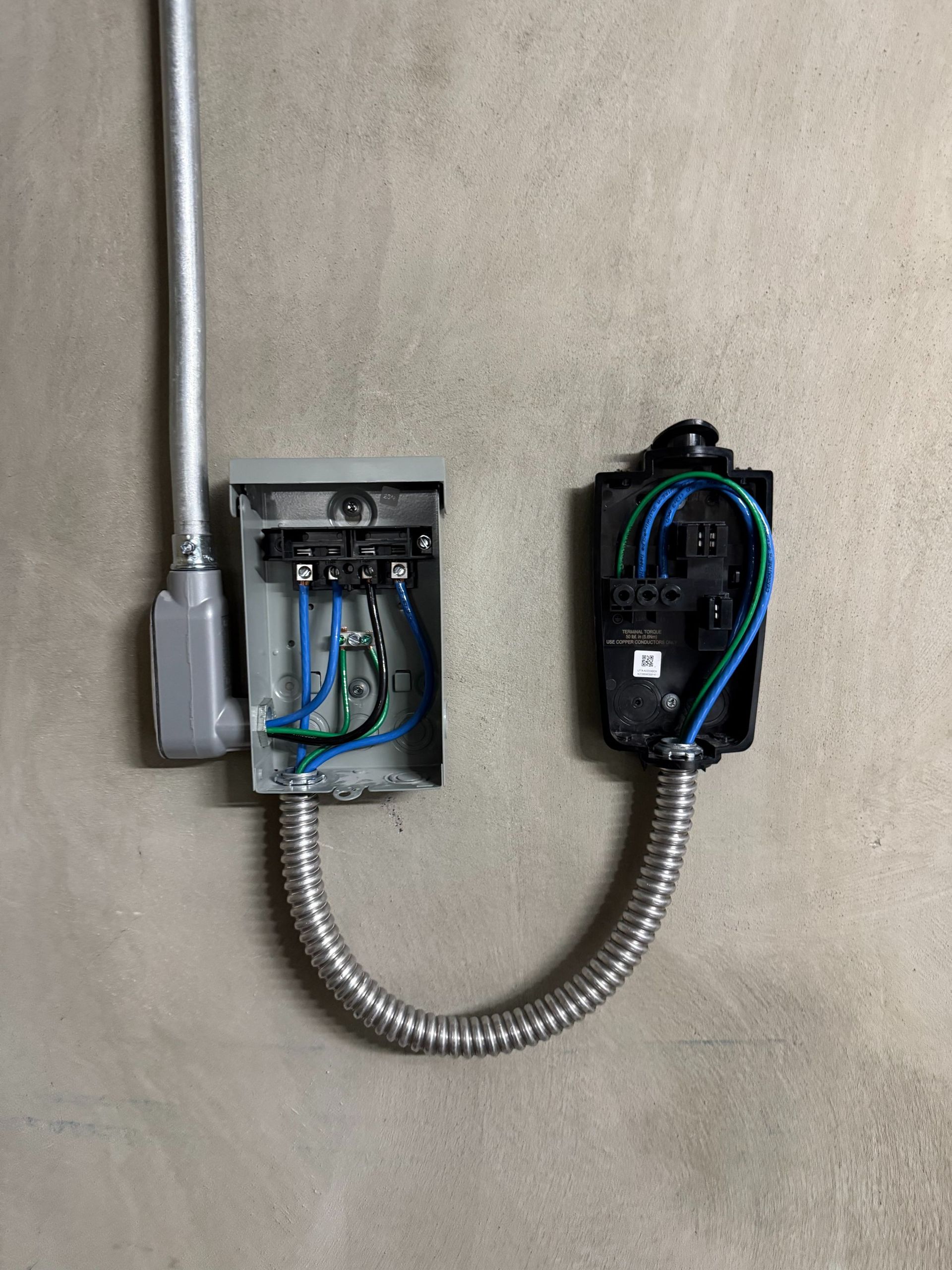 Two electrical junction boxes with exposed blue wiring connected by flexible metal conduit on a wall