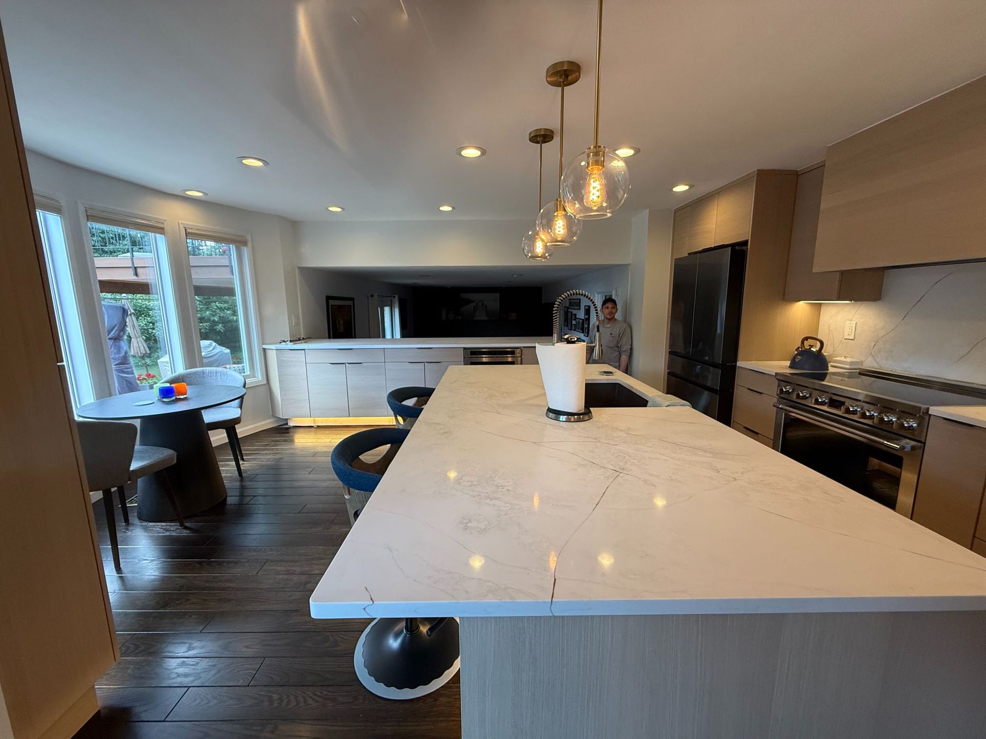 Modern kitchen with long island, marble countertop, pendant lights, and dark wood floors