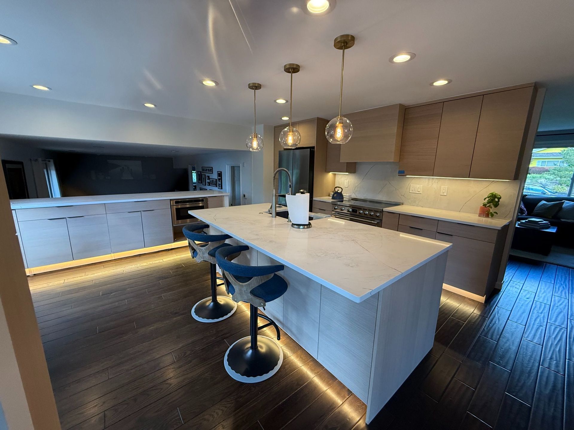 Modern kitchen with large white island, three bar stools, dark wood floors, and recessed lighting