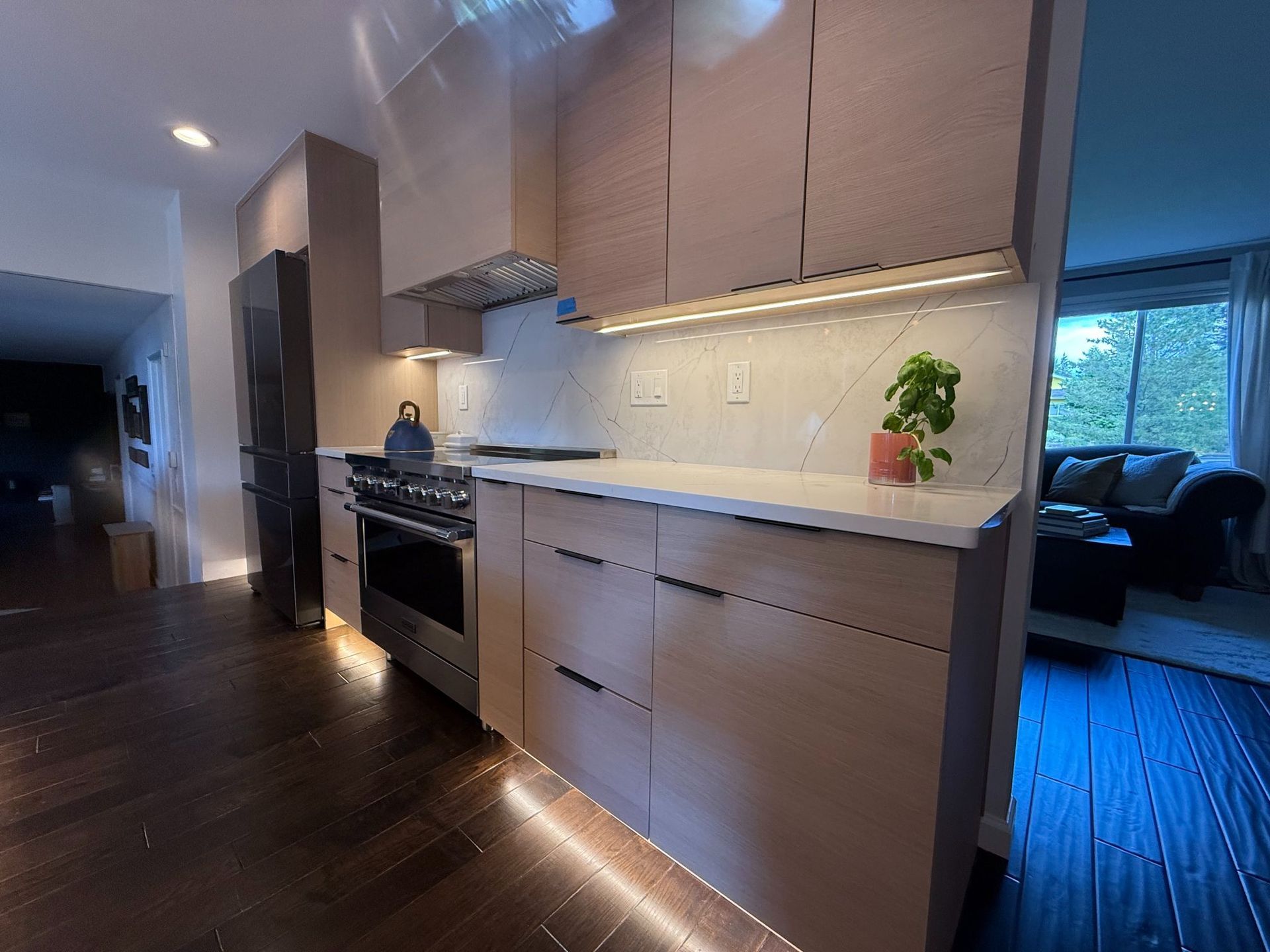 Modern kitchen with beige cabinets, stainless steel appliances, dark wood floors, and a view into a living room