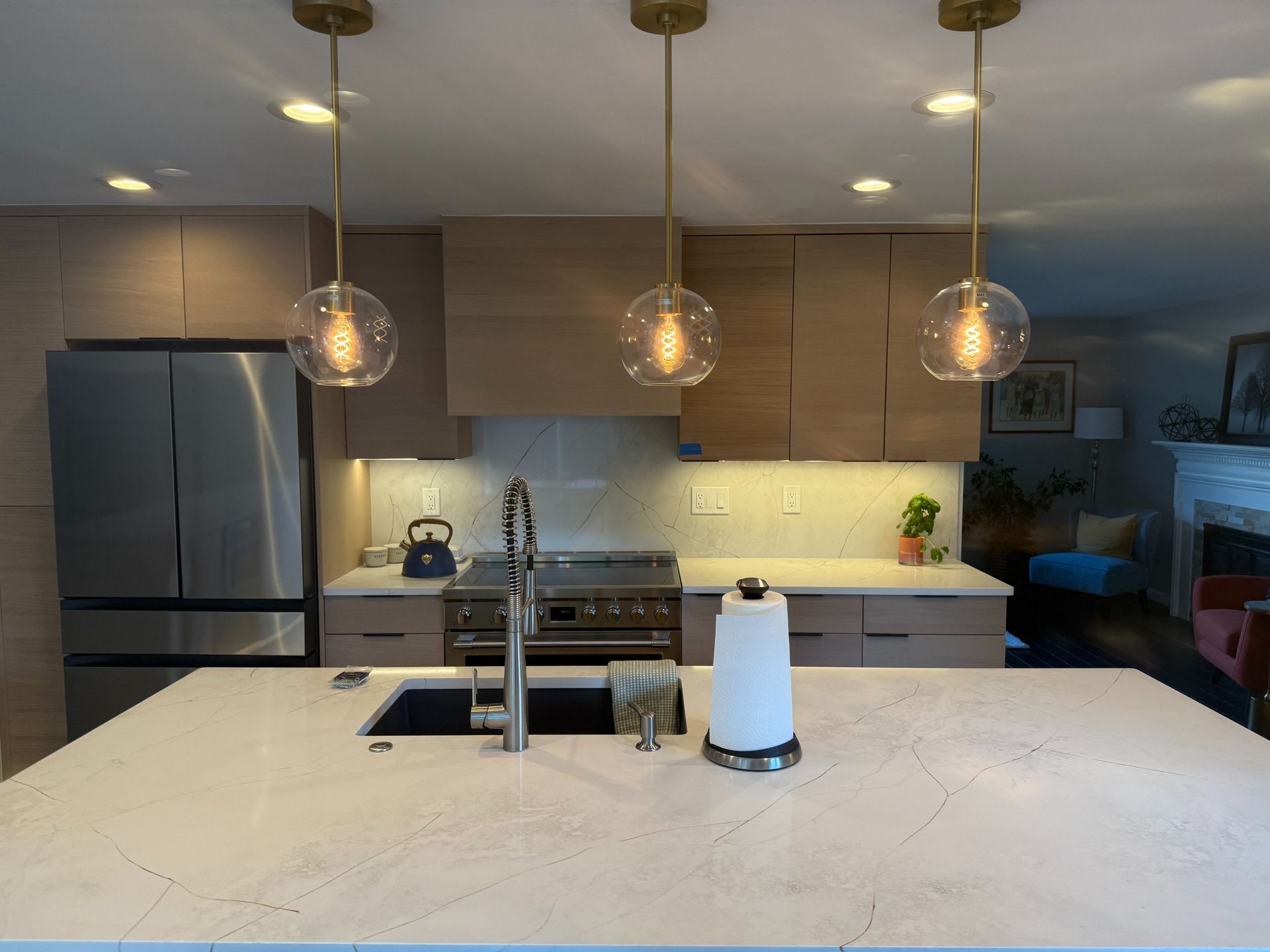 Modern kitchen with marble island, stainless fridge, pendant lights, and a paper towel roll on the counter