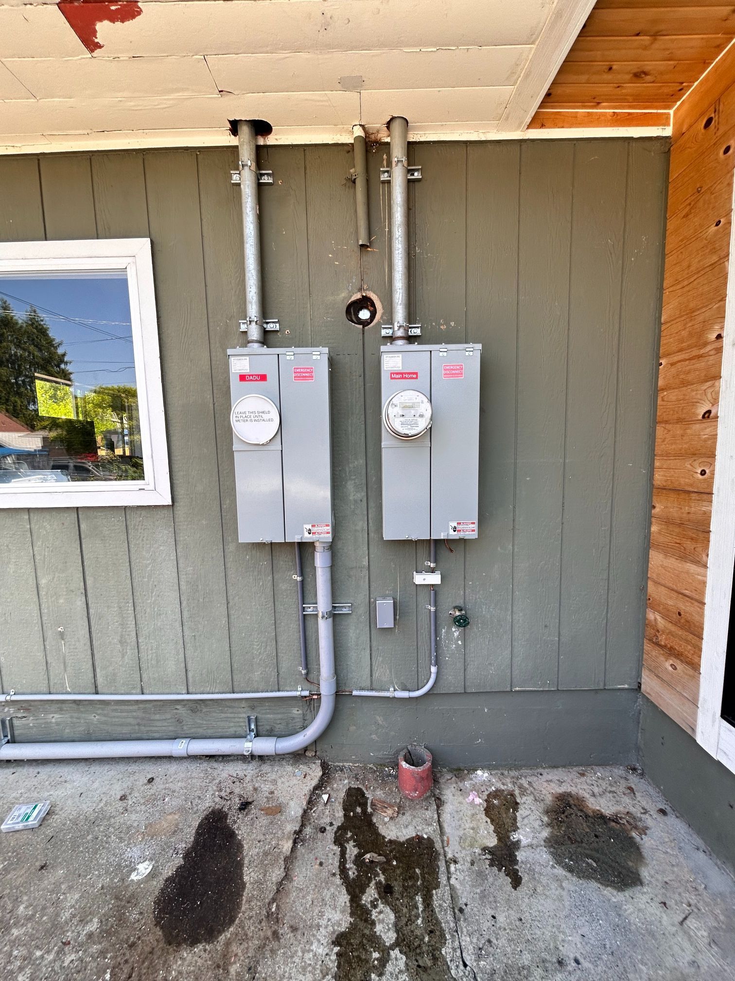 Two gray electrical meter boxes mounted on a building wall with conduit and wet stains below