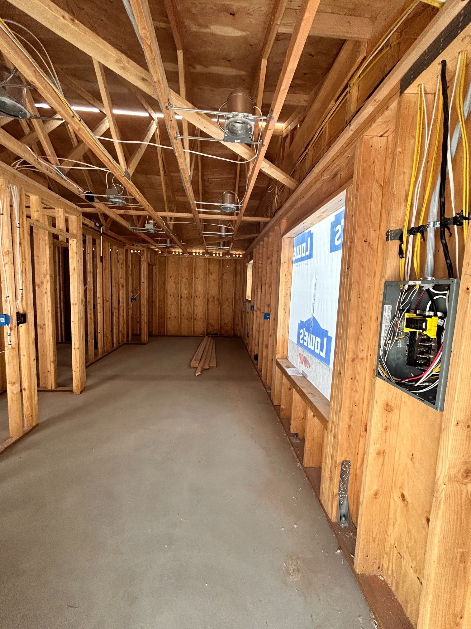 Unfinished room with exposed wood framing, concrete floor, and electrical wiring in a new home under construction