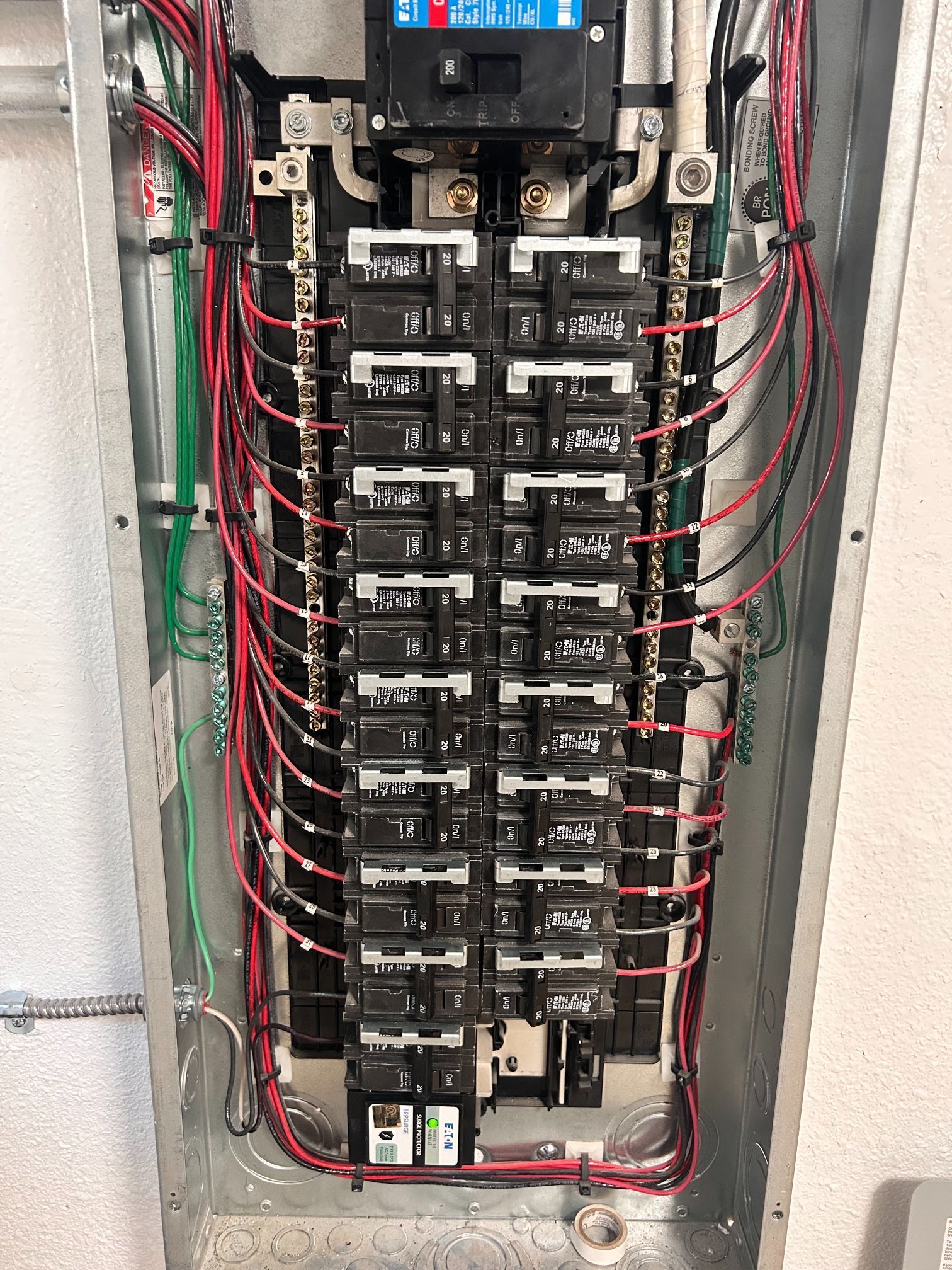 Open electrical breaker panel with rows of circuit breakers and red wiring in a wall recess