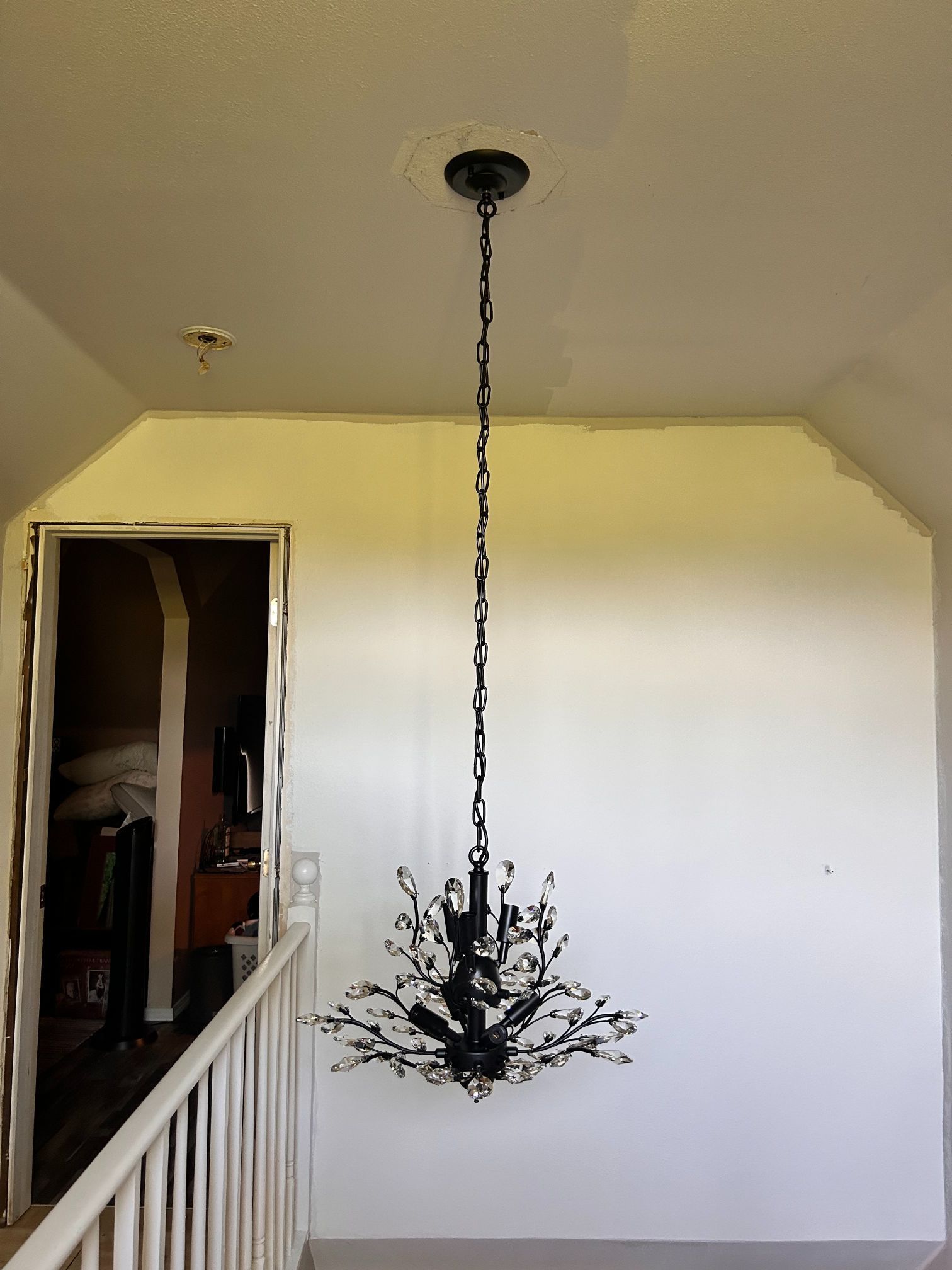 Hanging black chandelier in a bare room with yellow and white walls and a staircase railing.
