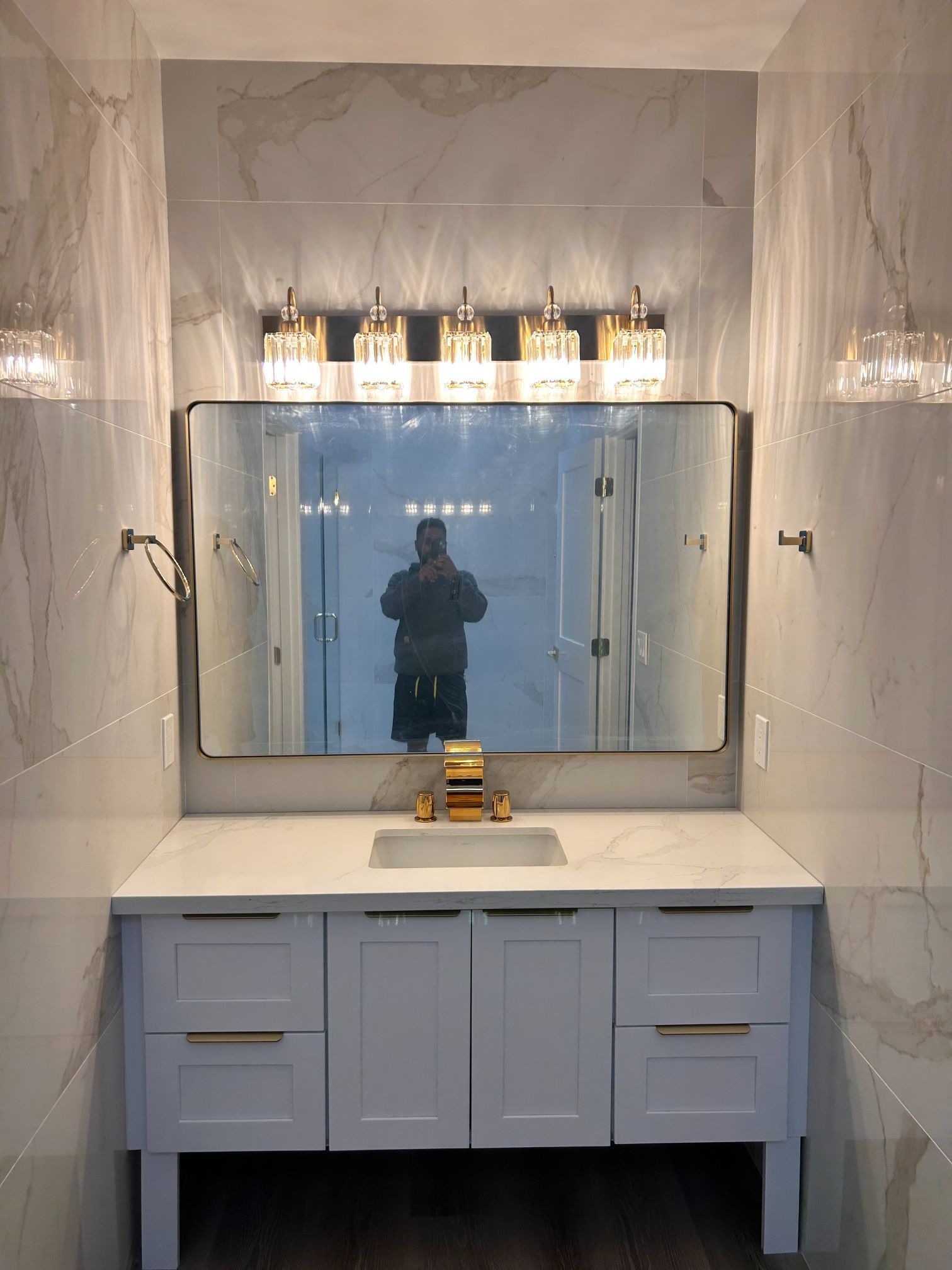 Bathroom vanity with marble countertop, large mirror, and pendant lights reflecting a person taking the photo