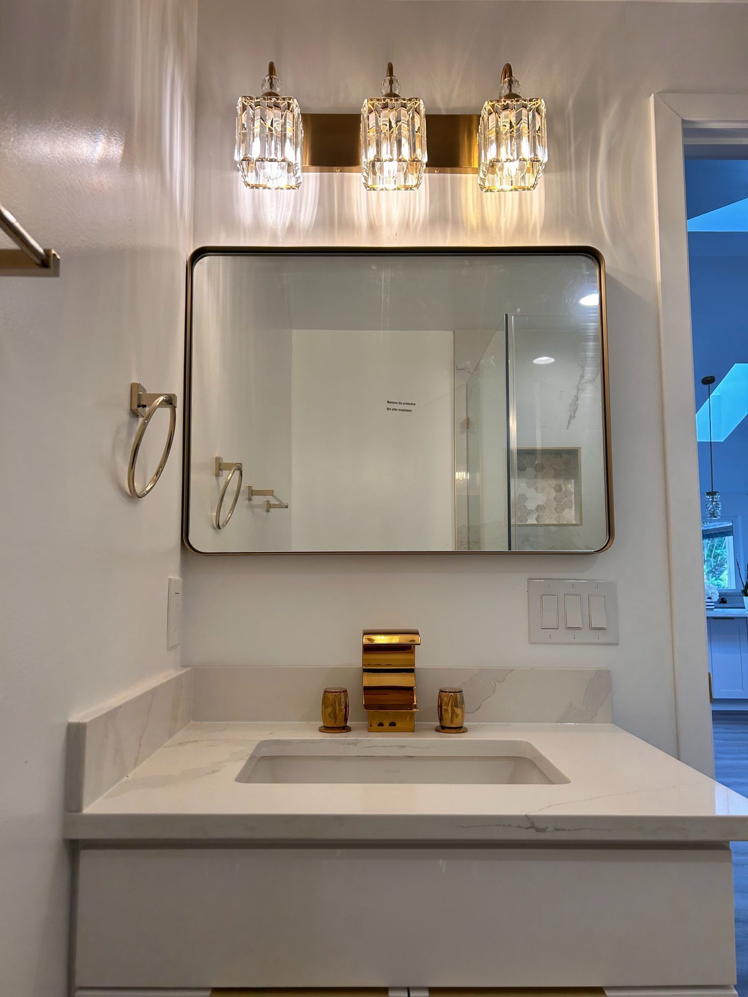 White bathroom vanity with mirror, triple light fixture, and built-in sink under a towel ring.