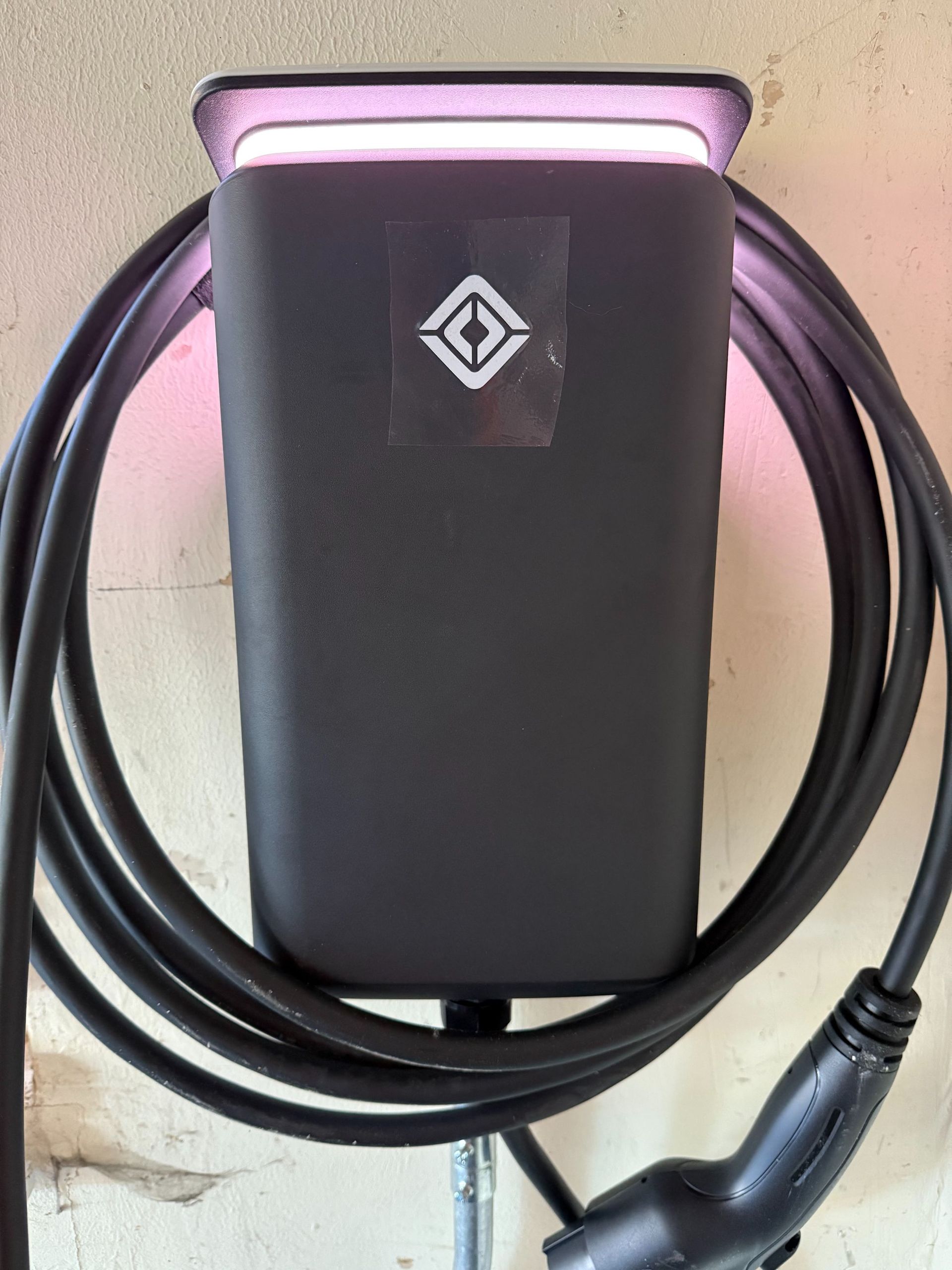 Black wall charger with coiled cable, lit by pink and purple light.