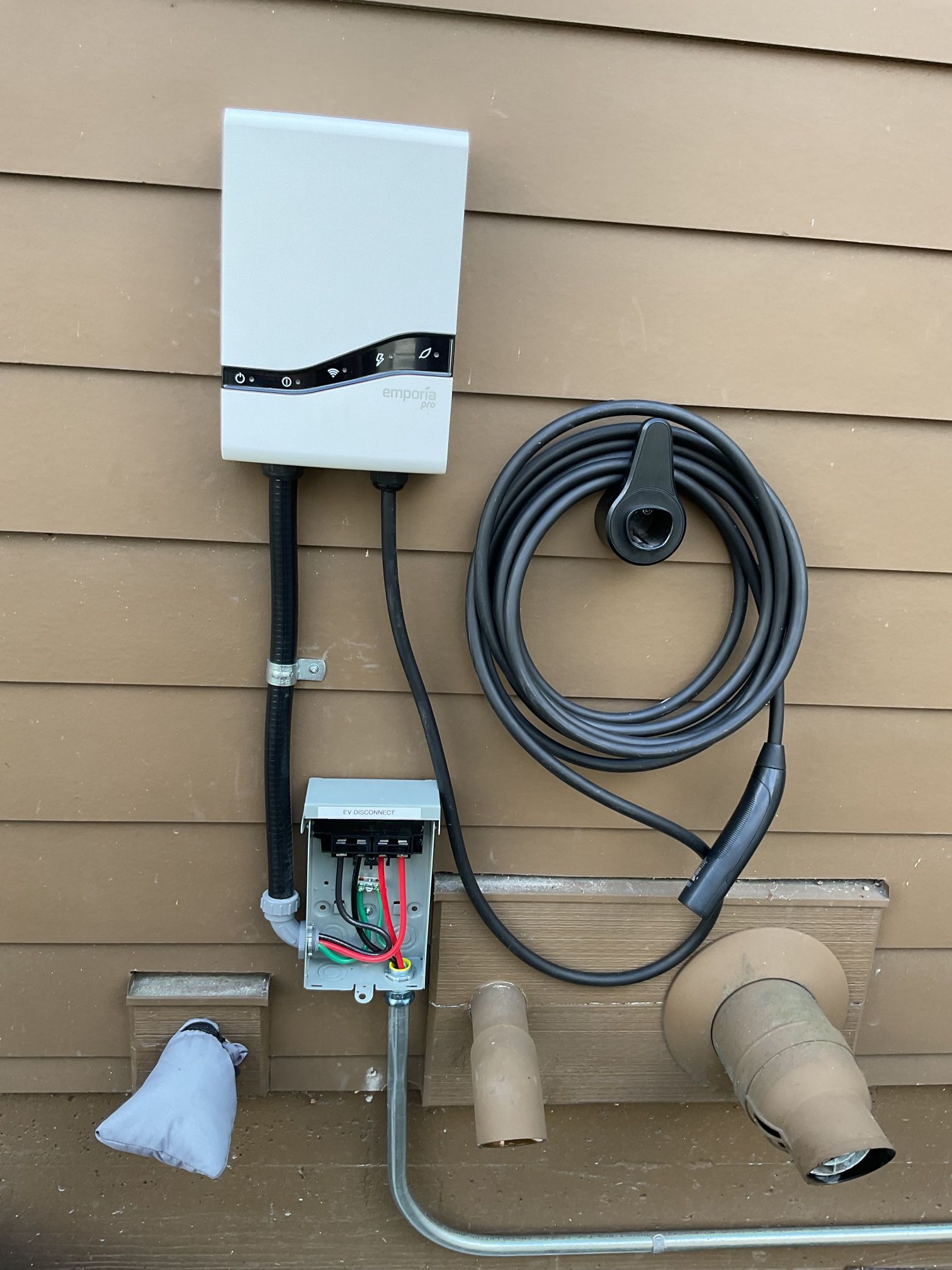 Outdoor electrical panel with coiled cable, junction box, and exposed wires mounted on house siding