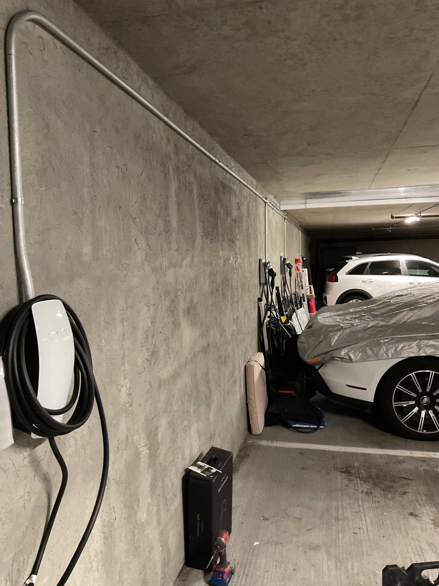 Indoor parking garage with a white car, wall-mounted hose, and stored tools along the side.