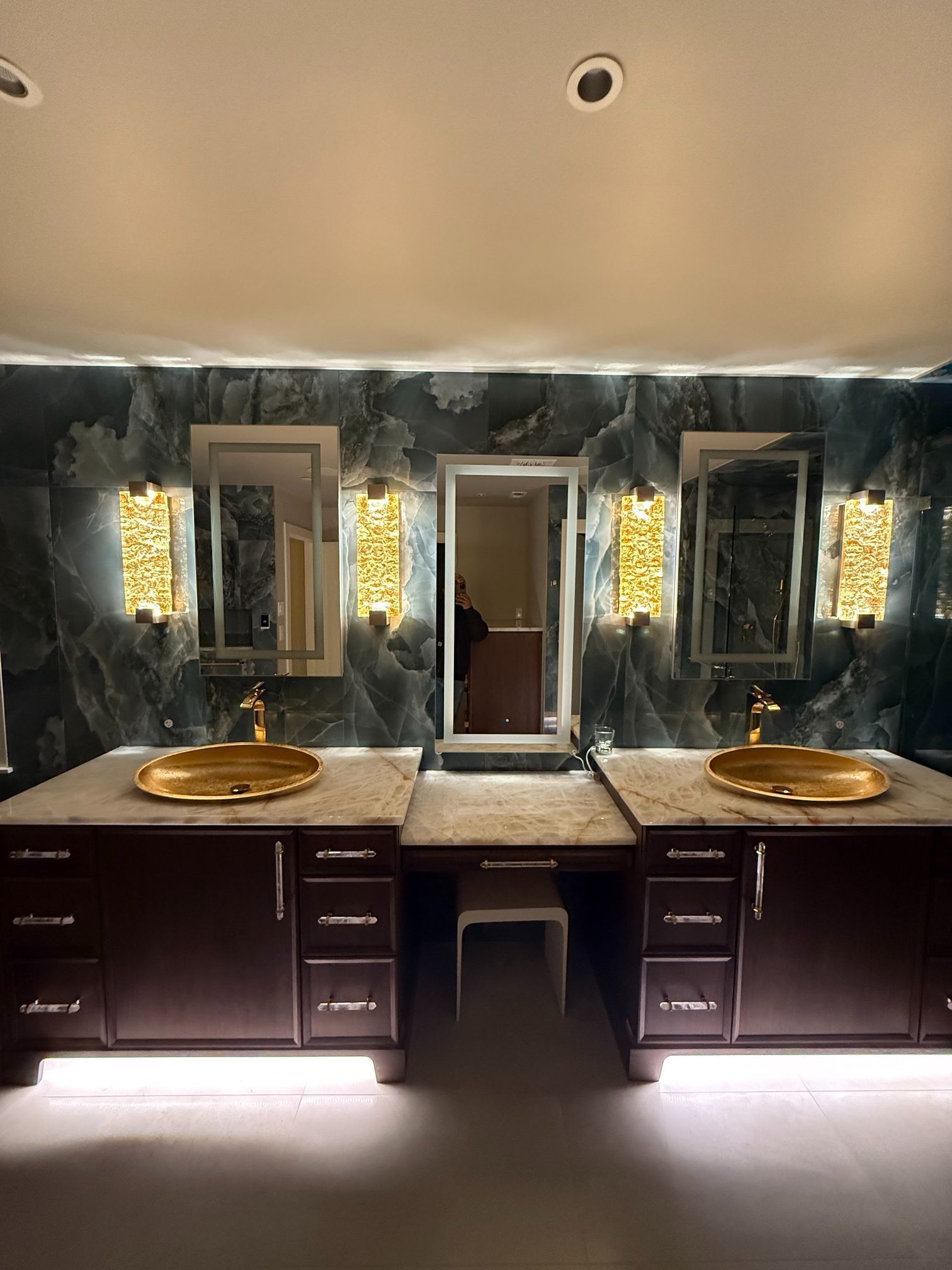Double vanity bathroom with dark wood cabinets, stone backsplash, and lit wall sconces
