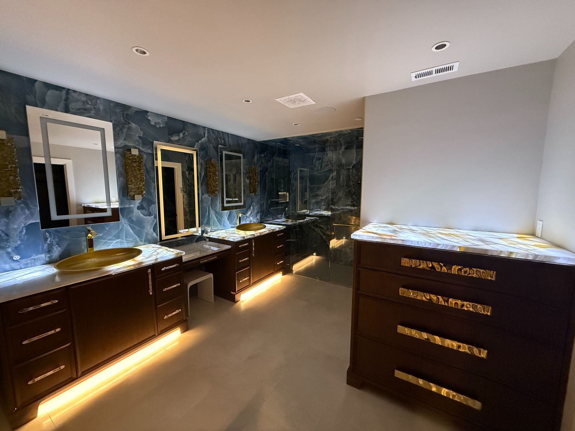 Modern bathroom with double vanities, large mirrors, dark cabinetry, and blue marble walls.
