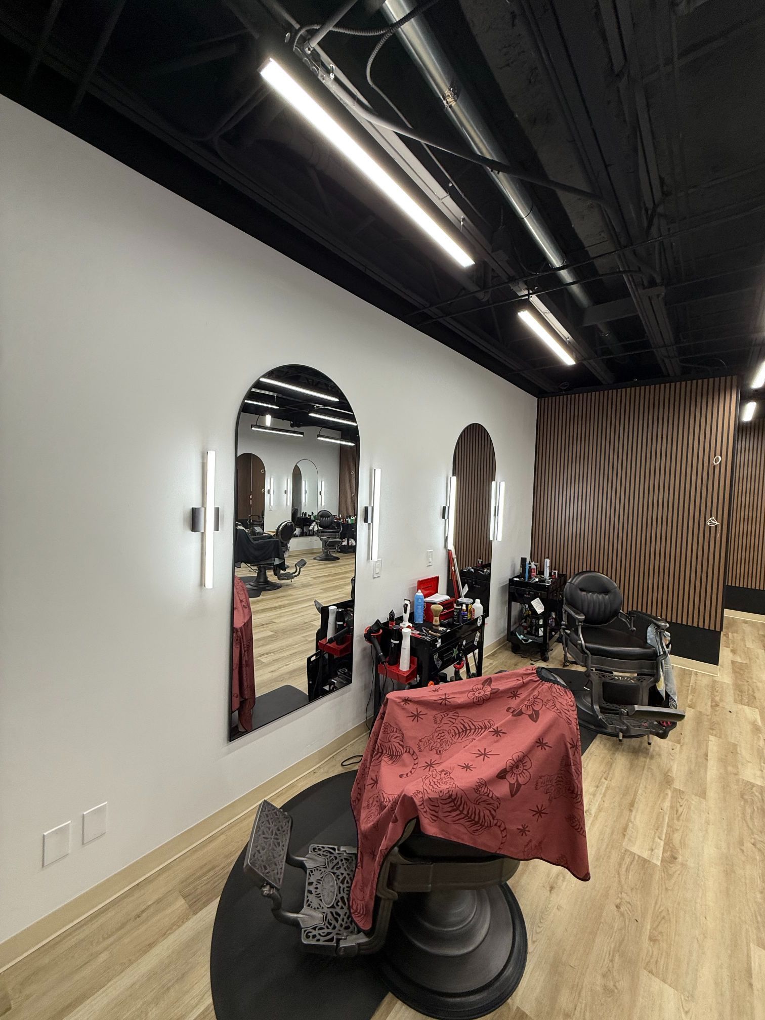Barber shop interior with mirrors, styling chairs, and a covered client chair on wooden floor