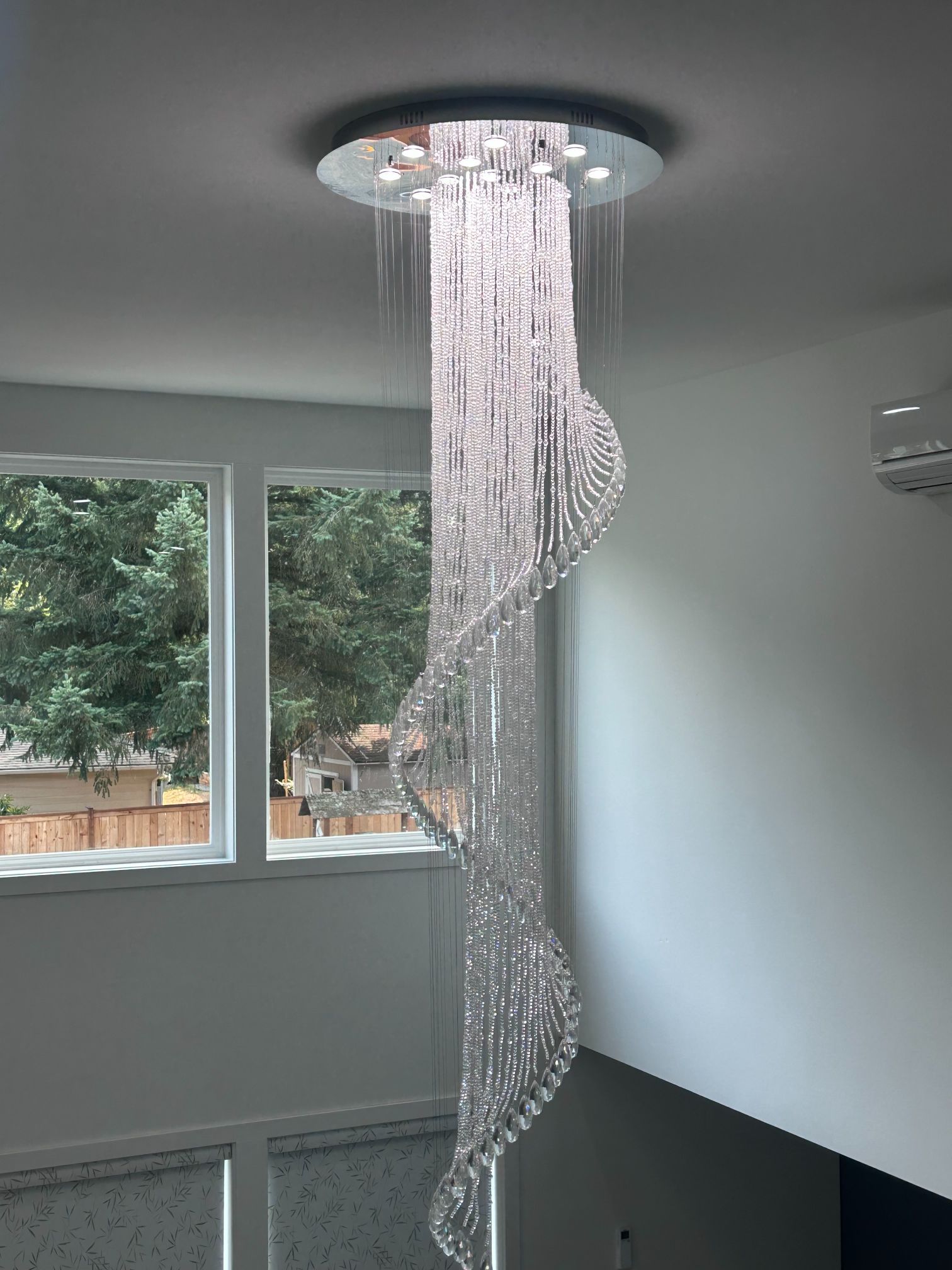 Crystal beaded ceiling light cascading in a spiral near two windows in a modern room
