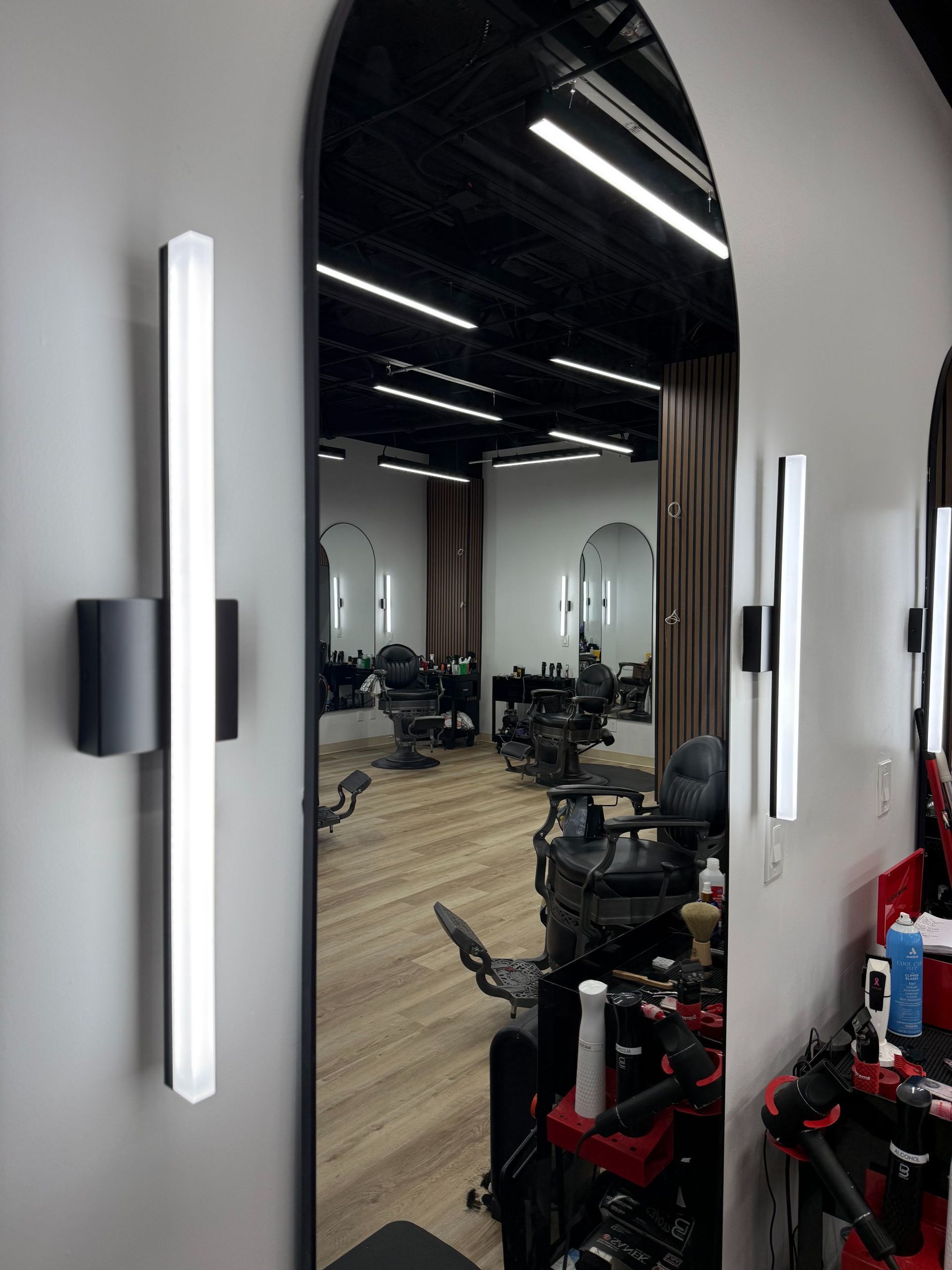 Salon mirrors and styling chairs beneath bright ceiling lights, seen through an arched doorway.