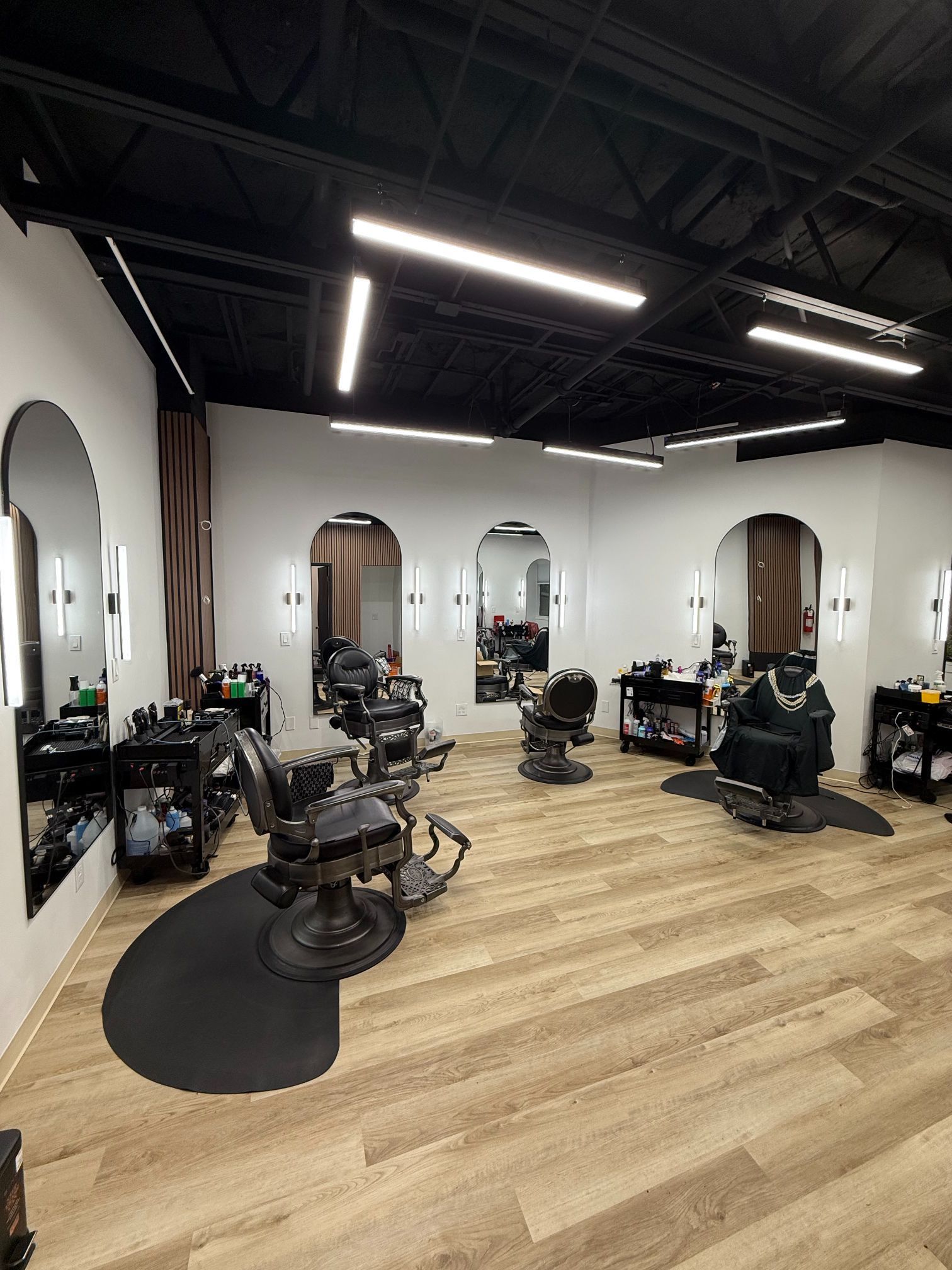 Modern barbershop interior with multiple black barber chairs and mirrors on wood flooring