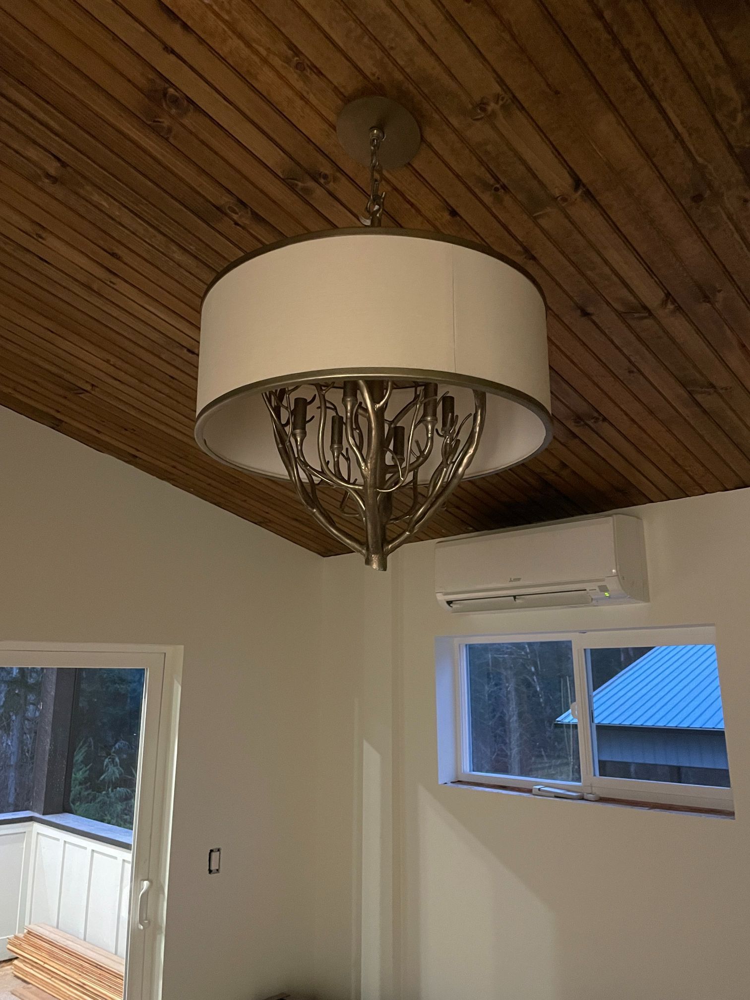Living room with a wood-paneled ceiling, chandelier, and two windows with an air conditioner.