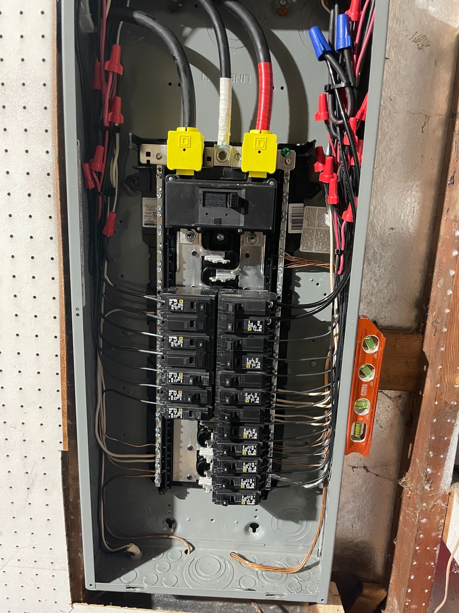 Open electrical breaker panel with black circuit breakers and red and black wires.