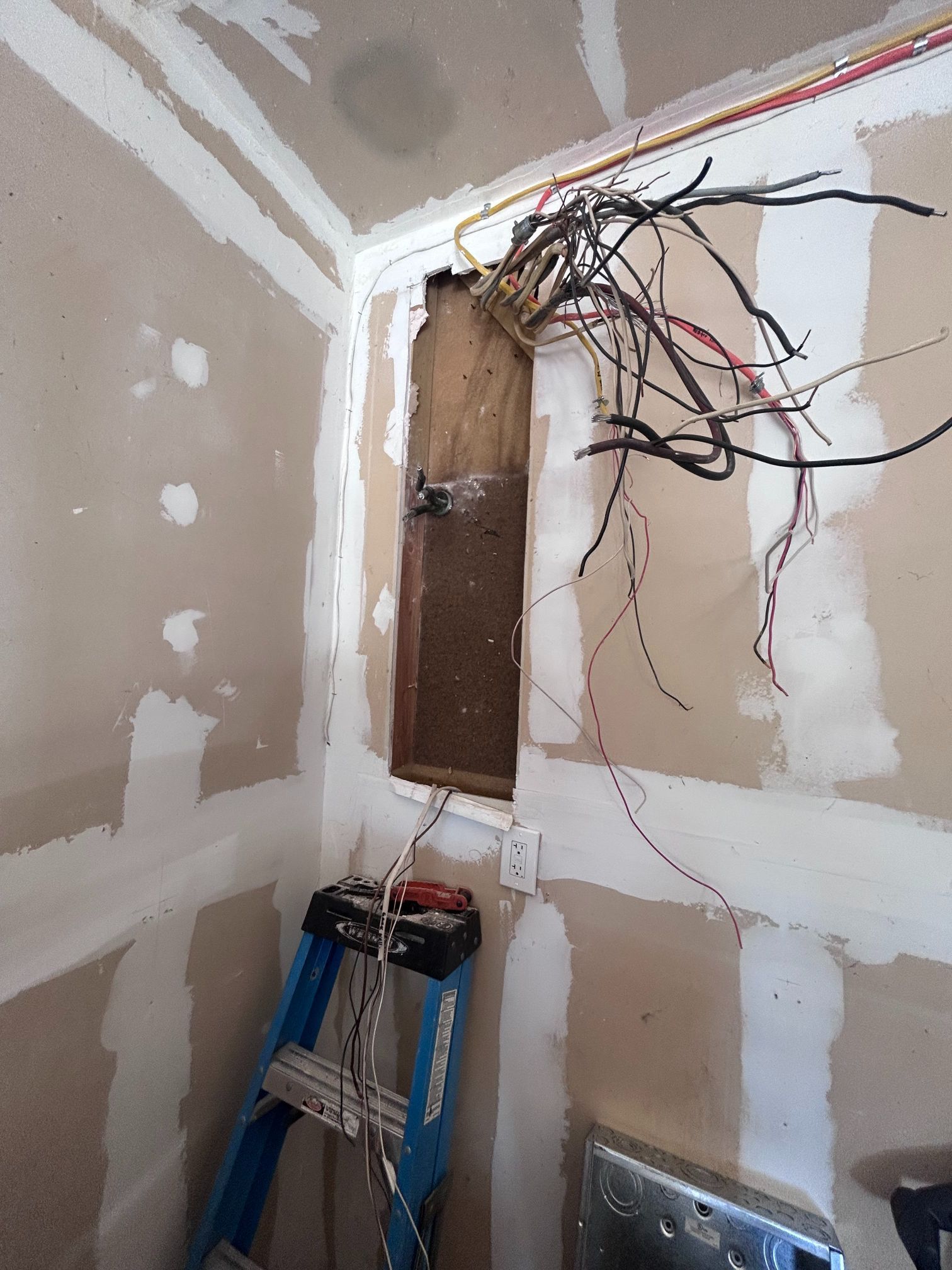 Exposed electrical wires in a damaged wall opening inside a partially renovated room.
