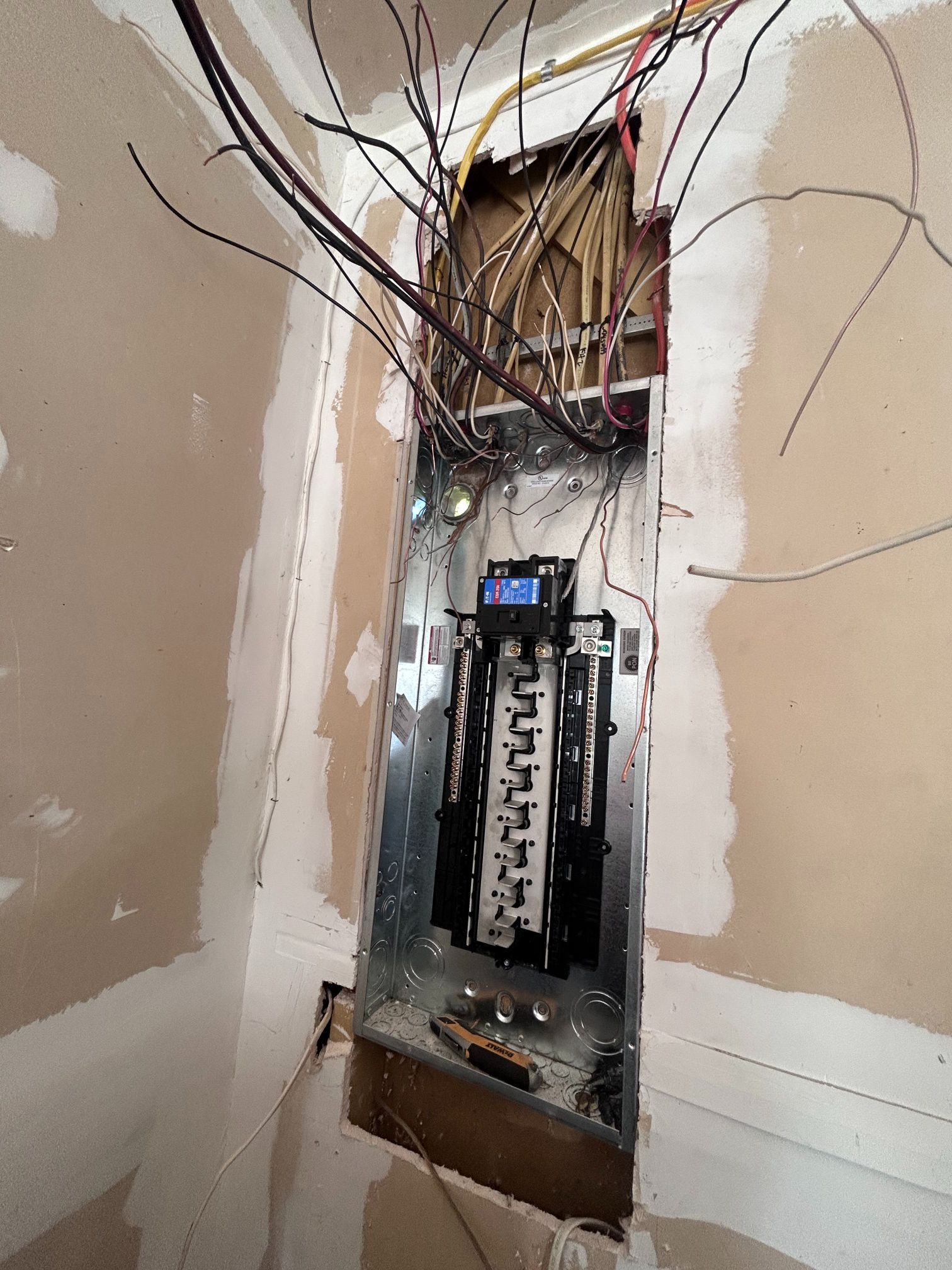 Open electrical breaker panel with exposed wiring and missing cover in a damaged wall opening