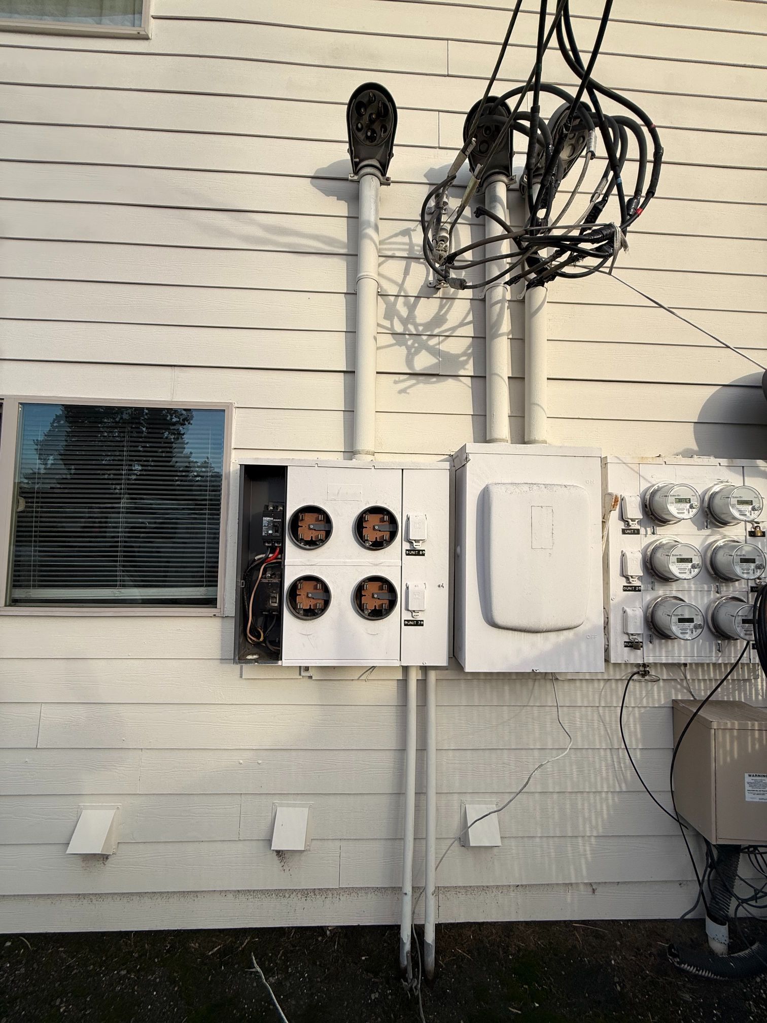 Utility meters and electrical boxes mounted on a beige building exterior with bundled cables above.