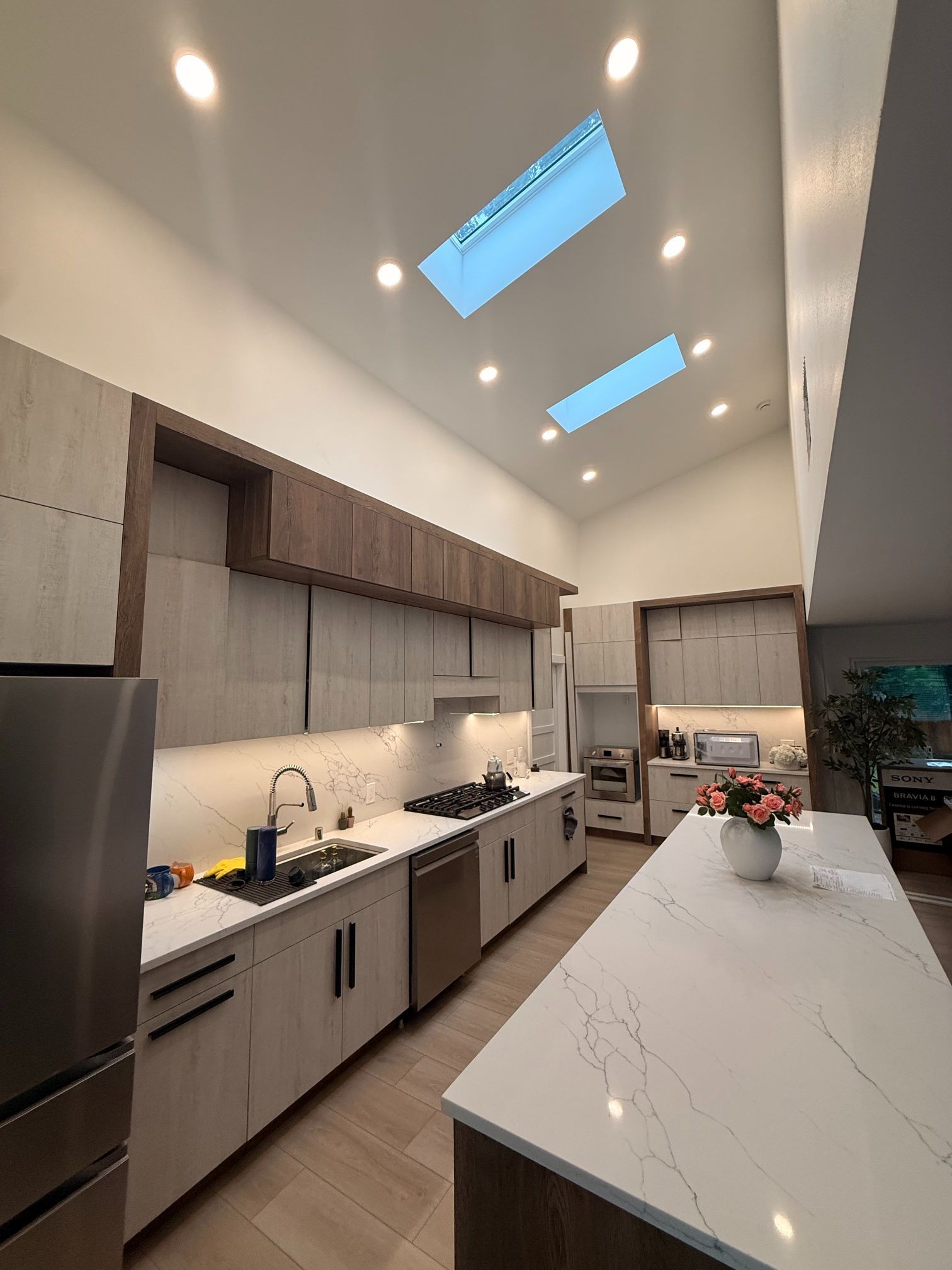 Modern kitchen with white marble island, wood cabinets, skylights, and a vase of flowers on the counter