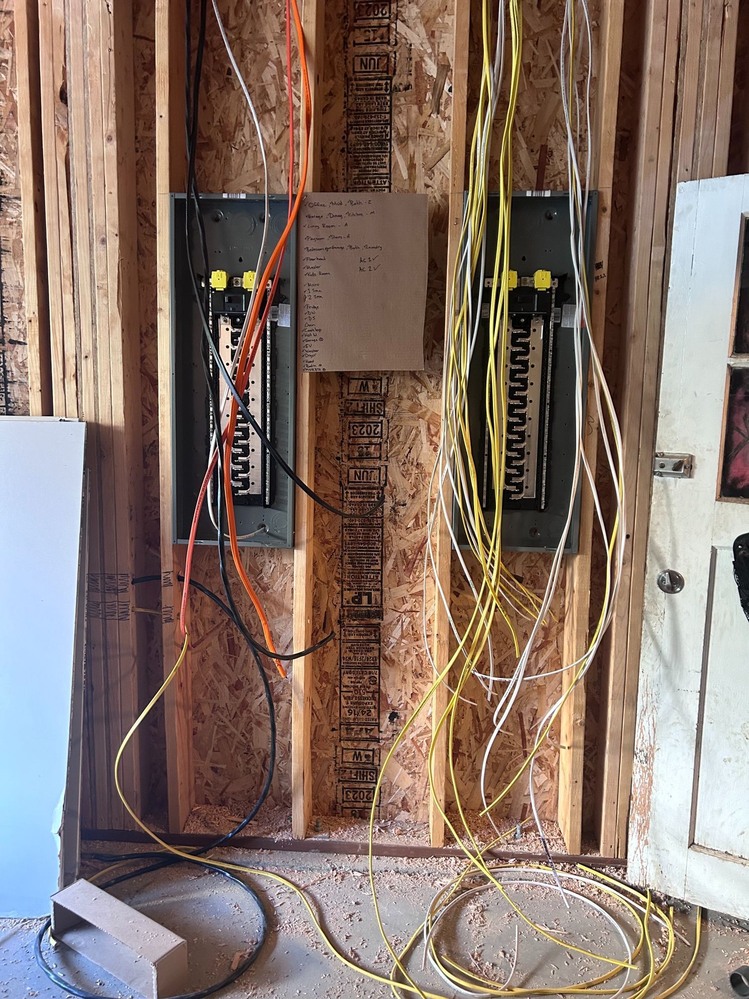 Two electrical panels with exposed wires in an unfinished wall cavity
