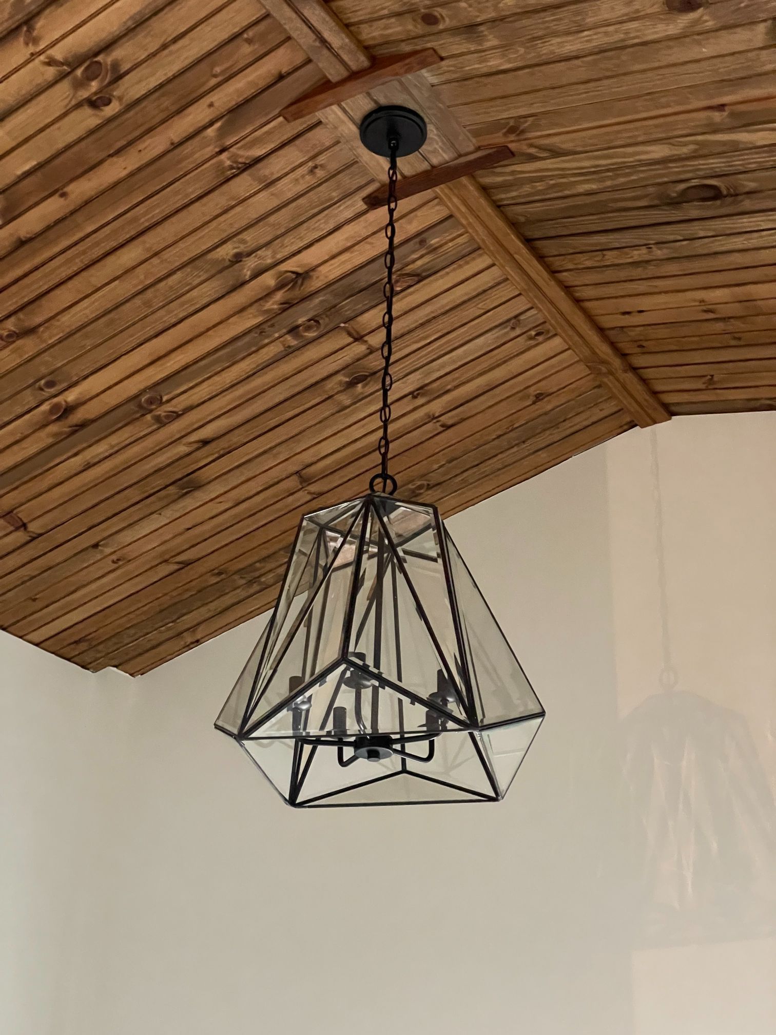Geometric black pendant light hanging from a wooden slat ceiling in a modern room