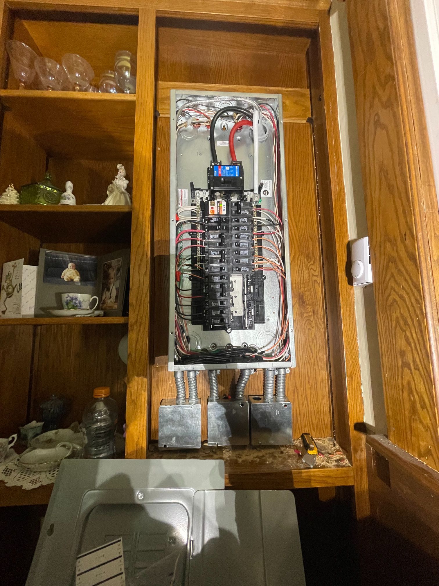 Open electrical panel mounted inside a wooden cabinet with exposed wiring and breakers