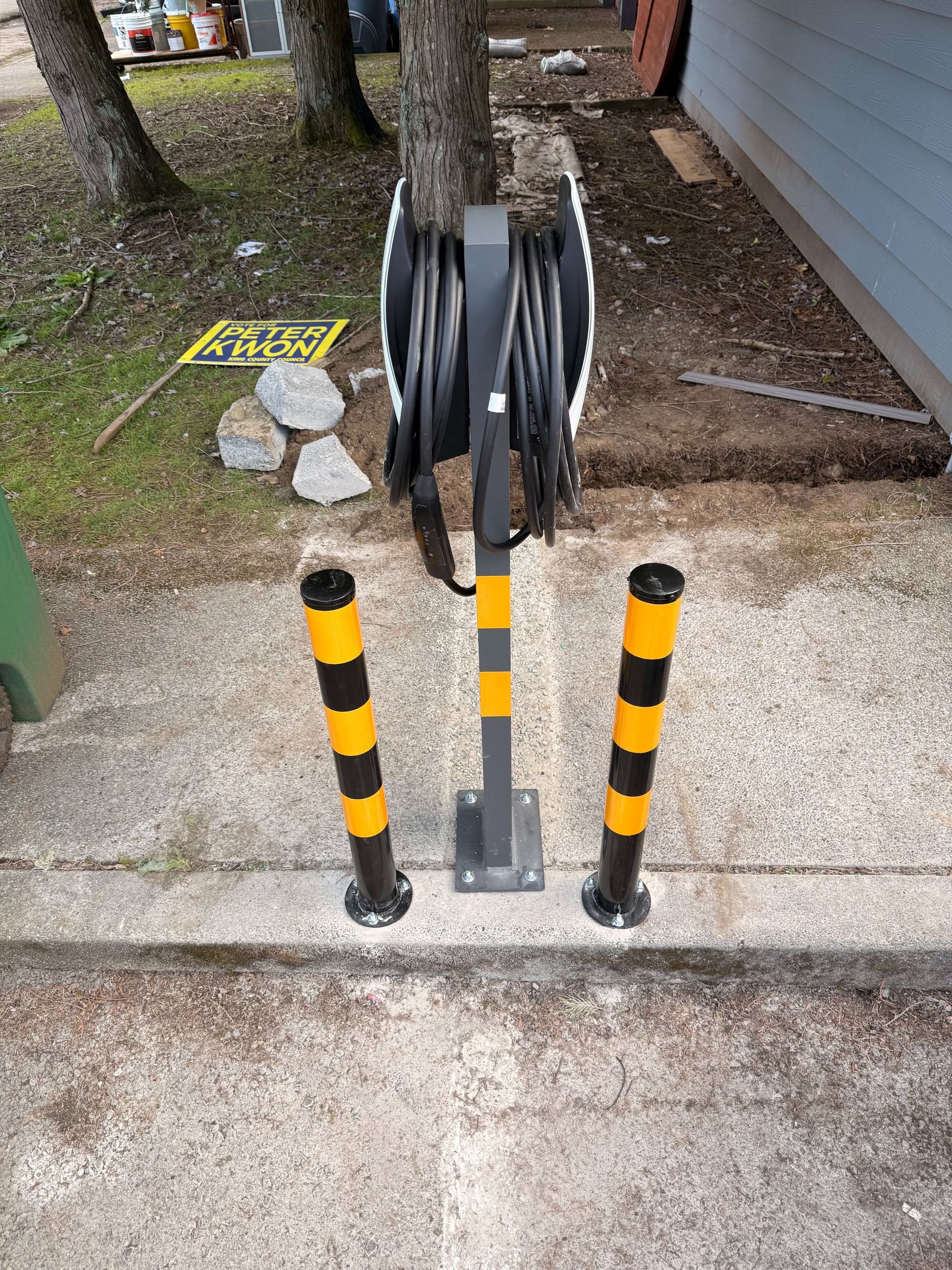 Spool rack with black hose reels between yellow-black bollards on a concrete pad outdoors.