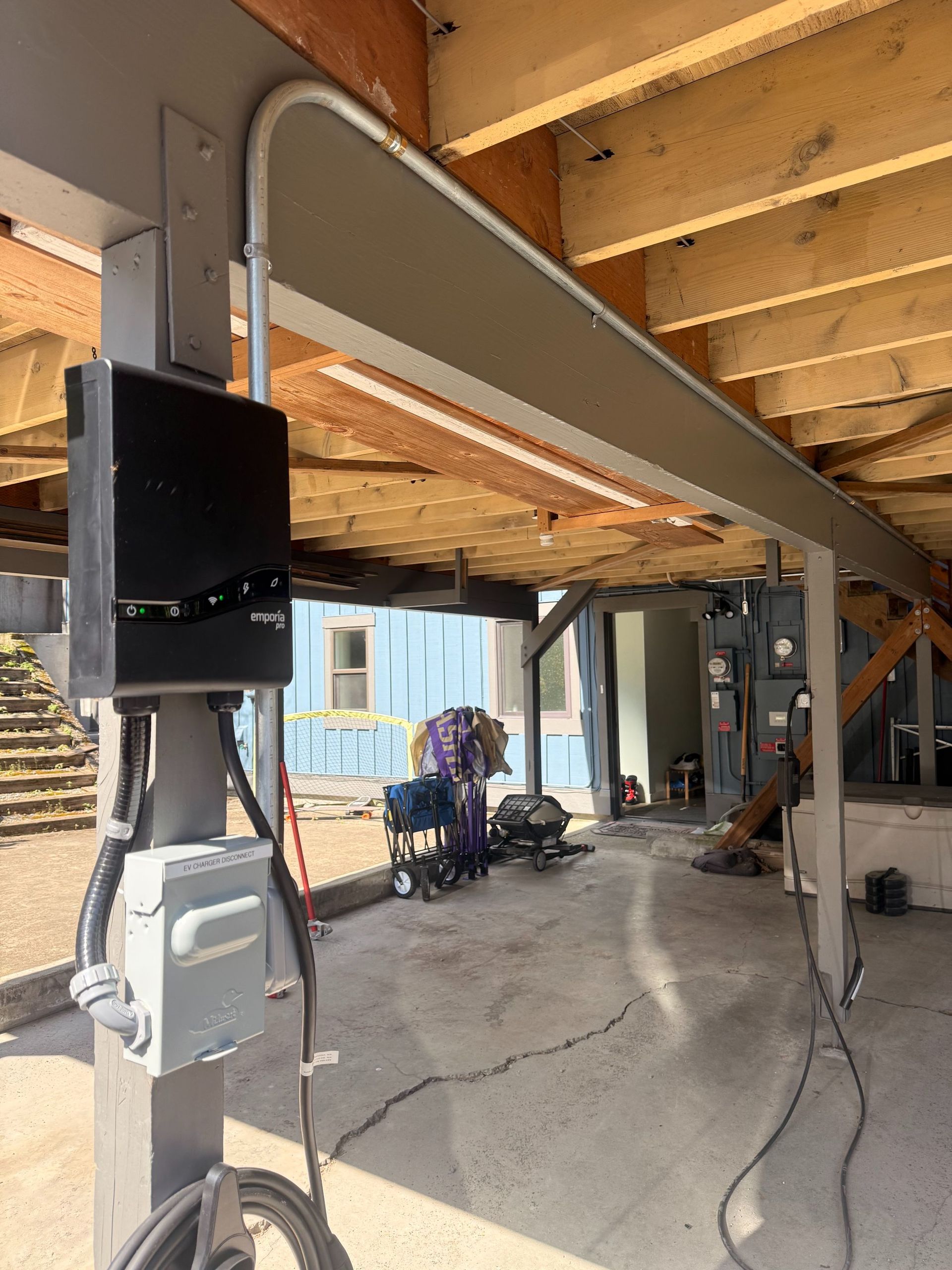 Construction area under a raised house with exposed beams, ducts, and tools on a concrete floor.