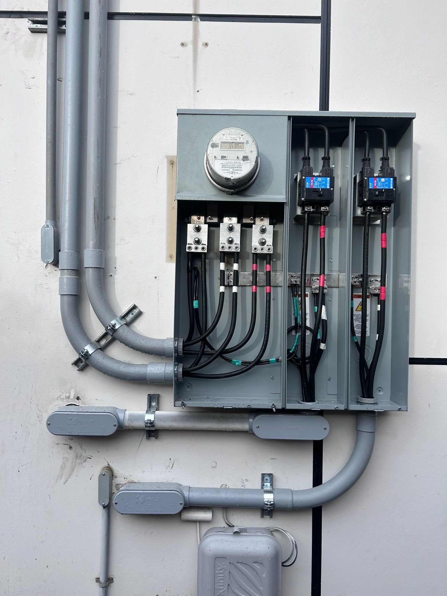 Electrical meter and circuit panel on a wall with conduit and gray utility boxes