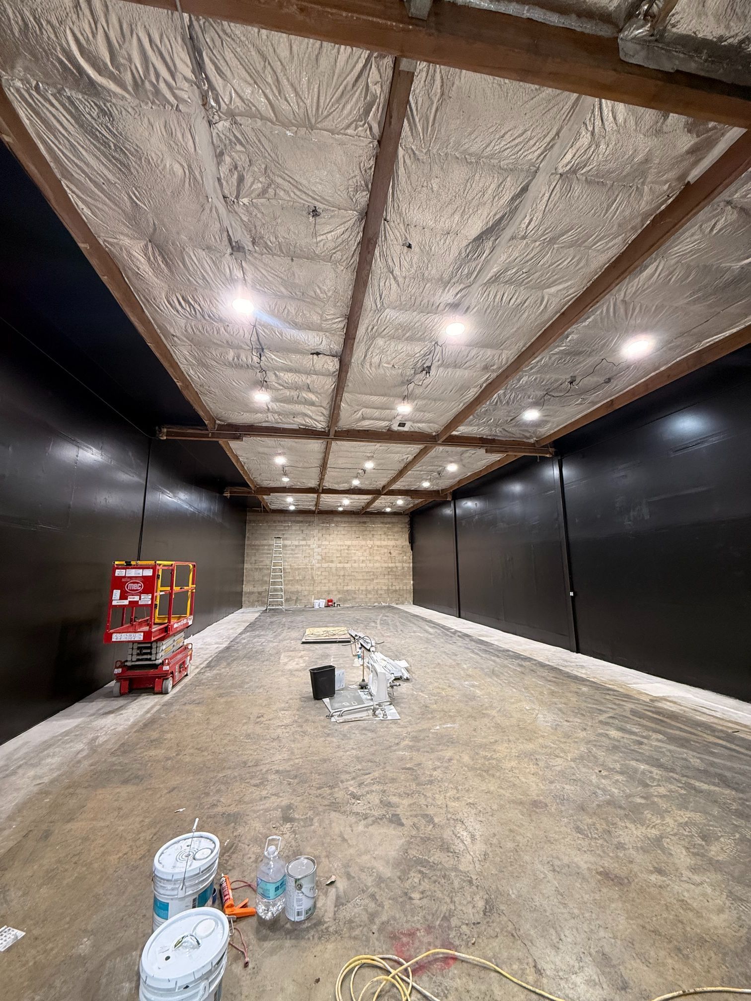 Empty room under construction with black walls, insulated ceiling, and a scissor lift on the left