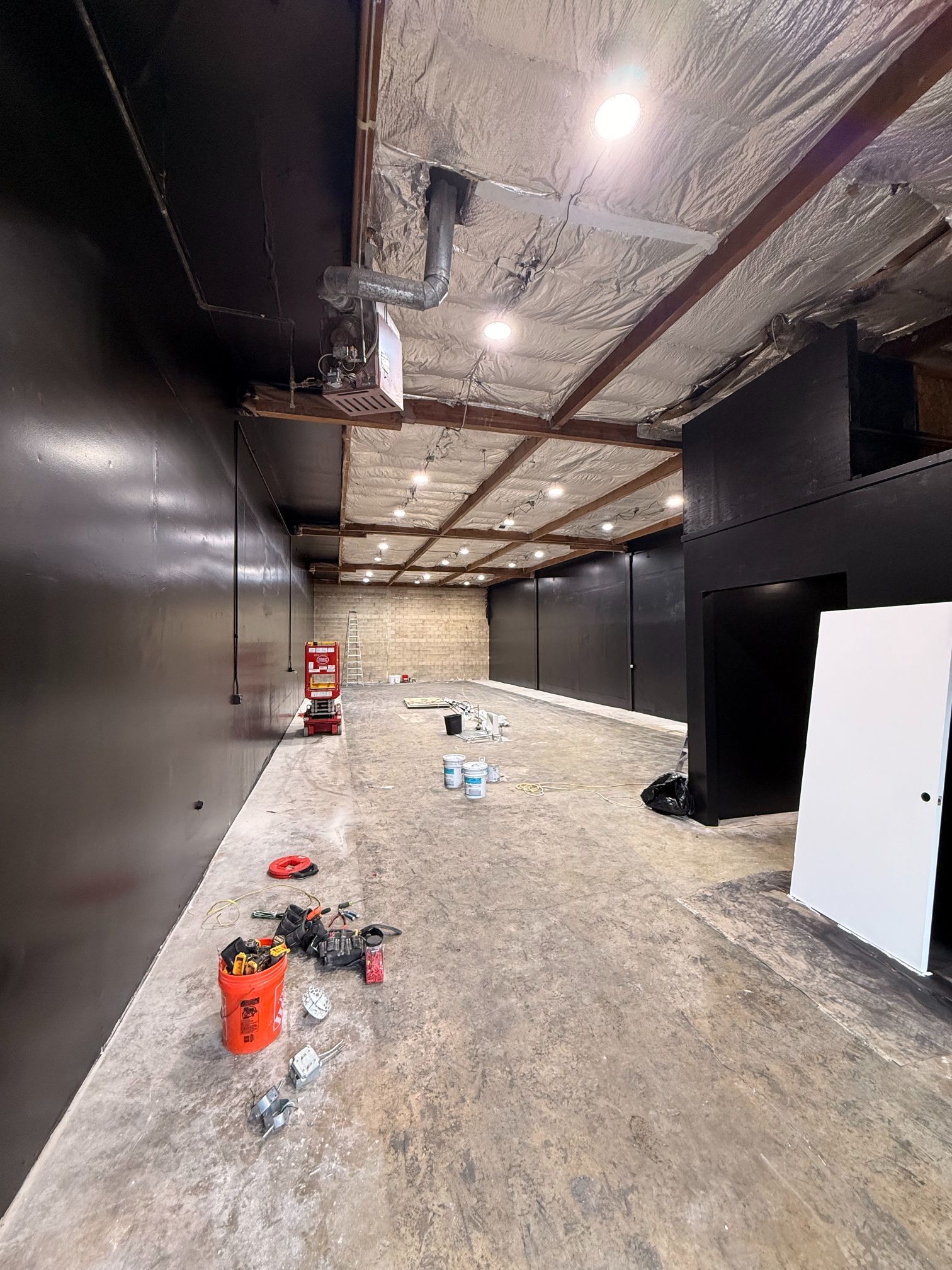 Vacant industrial interior with dark walls, exposed ceiling, and construction tools scattered on the concrete floor.