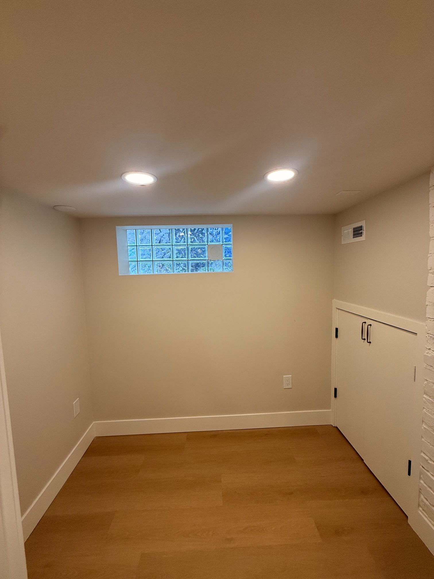 Small empty room with wood floor, beige walls, recessed lights, and a narrow window.