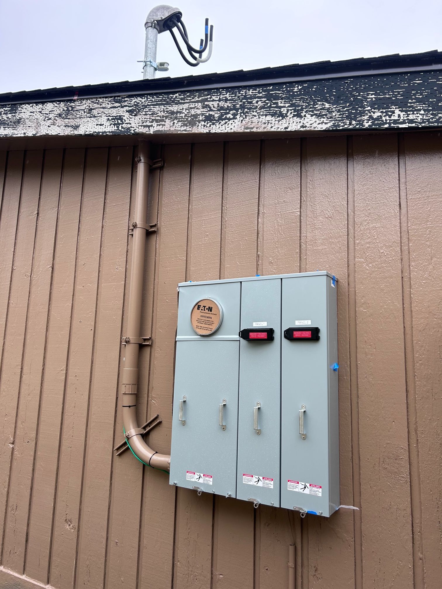 Two gray utility meter boxes mounted on a brown building wall under a dark roofline.