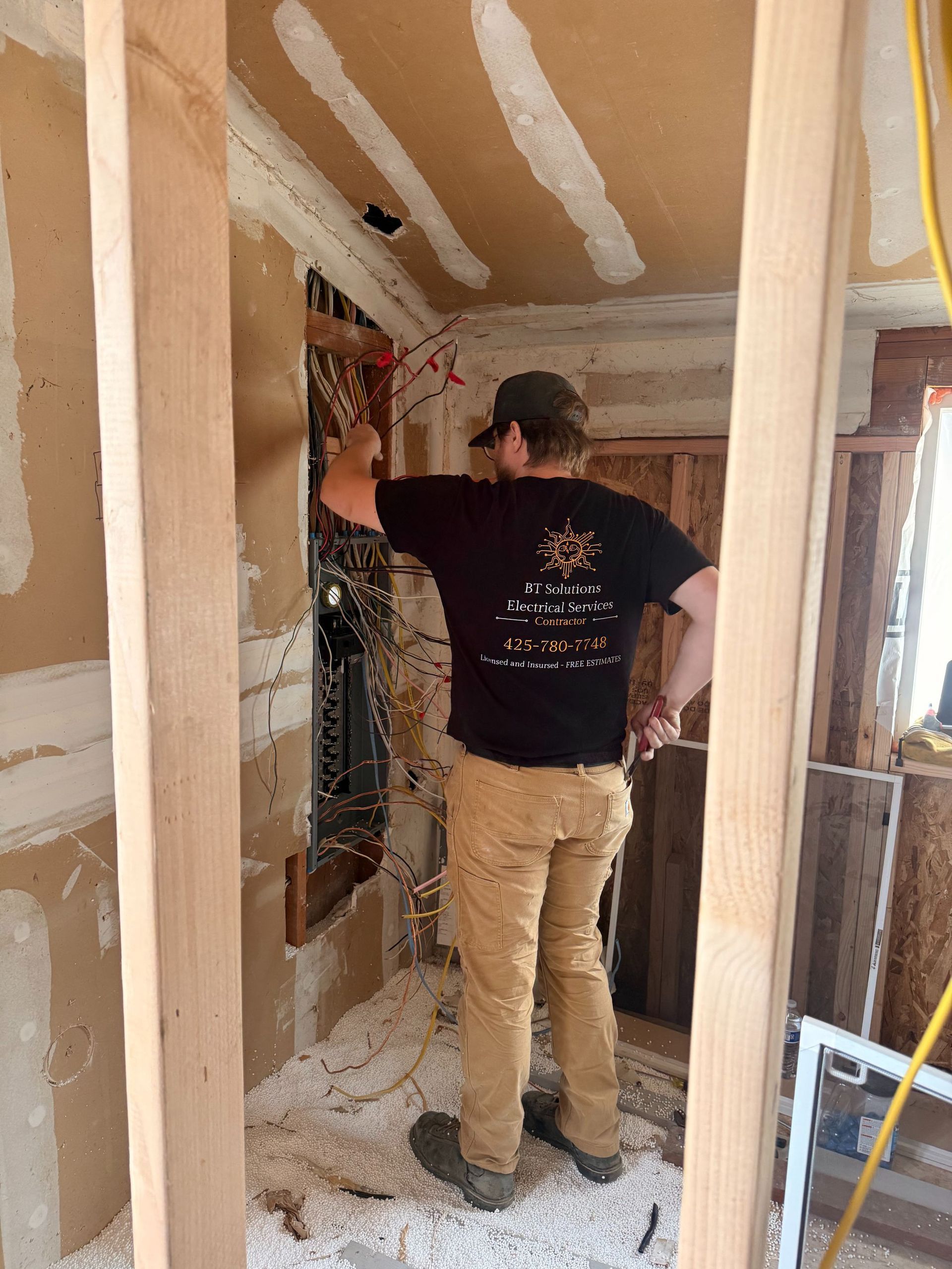 Worker standing in a narrow renovation hallway, inspecting exposed wiring and insulation.