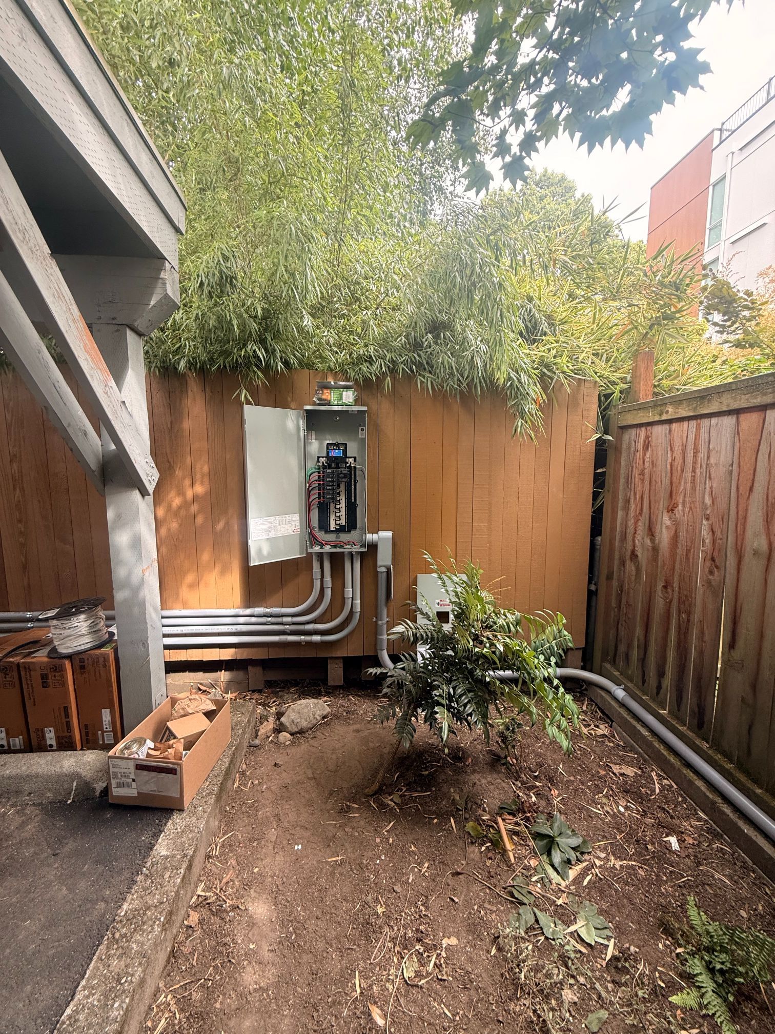 Small backyard with dirt bed, wooden fences, shrubs, and a utility meter against the far fence.