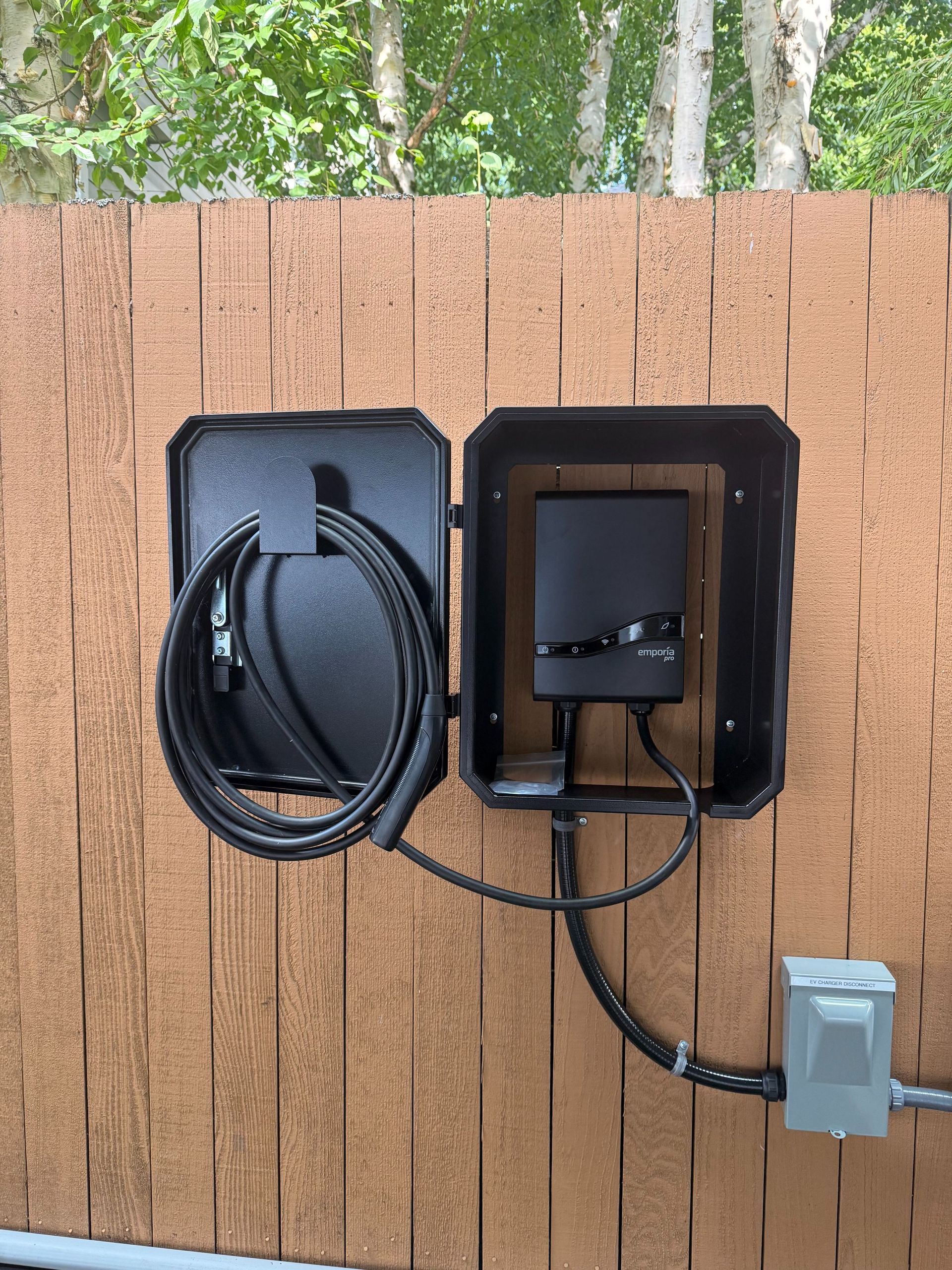 Outdoor wall-mounted utility box with coiled cable and electrical conduit on a wooden fence