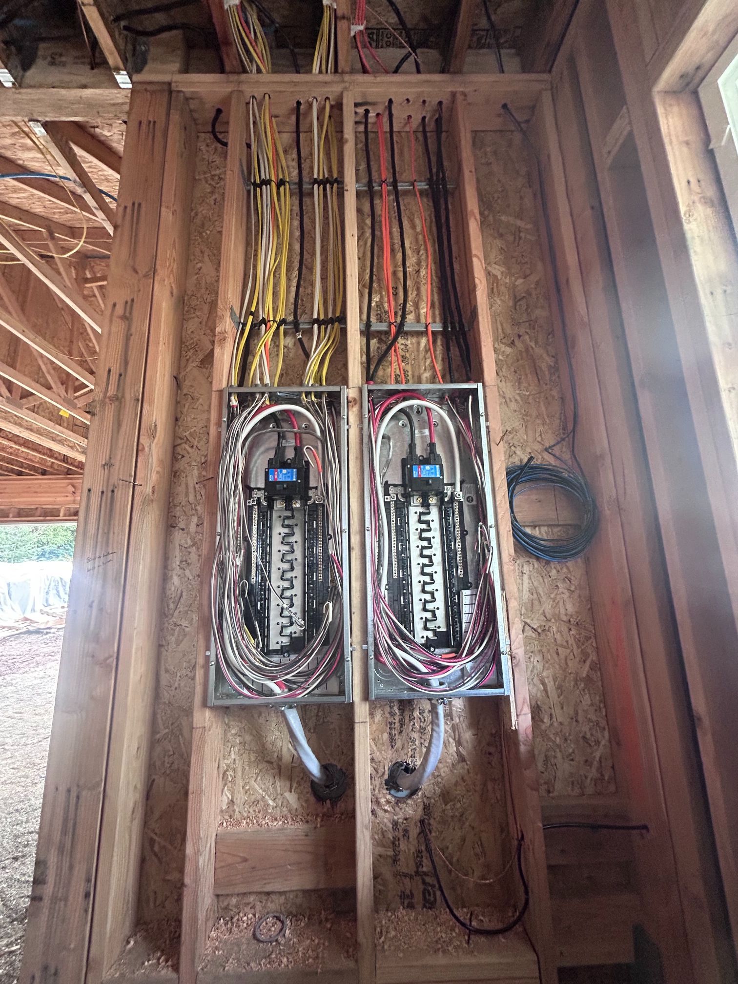 Two electrical breaker boxes mounted on a wooden wall inside an unfinished building.