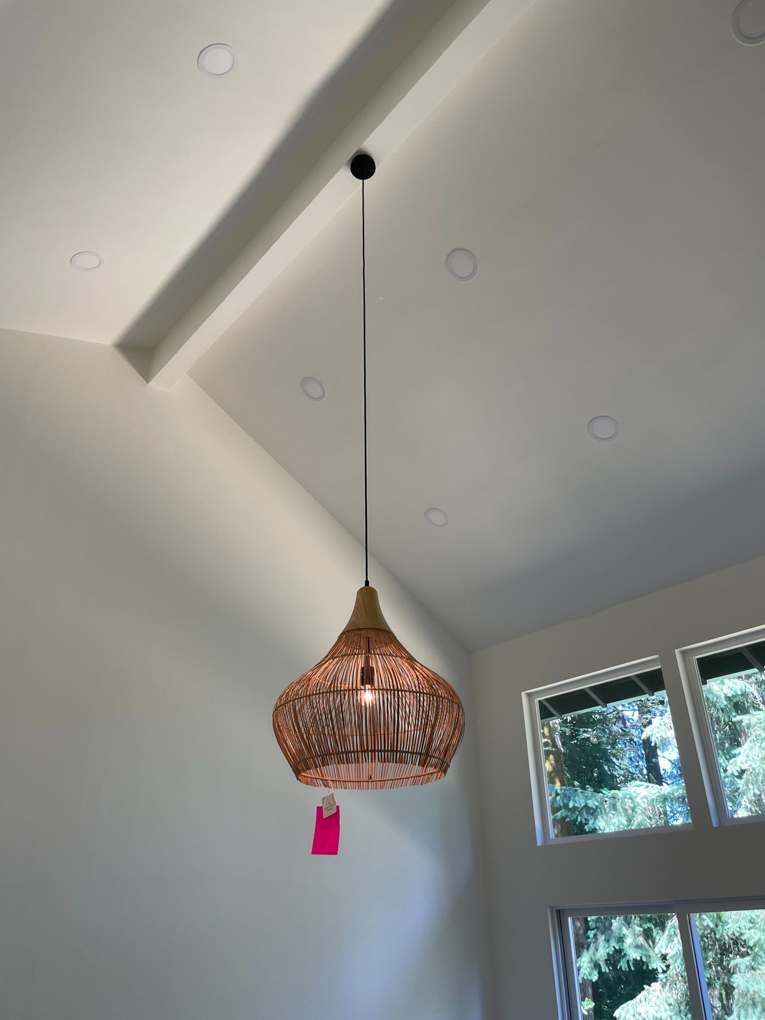 Woven pendant light hanging from a vaulted white ceiling near a window.