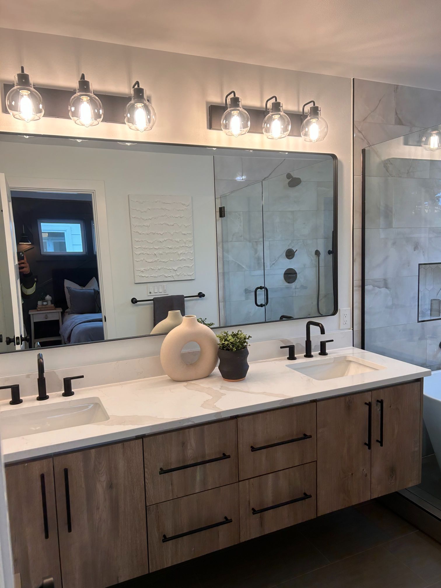 Modern bathroom vanity with large mirror, three light fixtures, and double sinks in a neutral-toned space