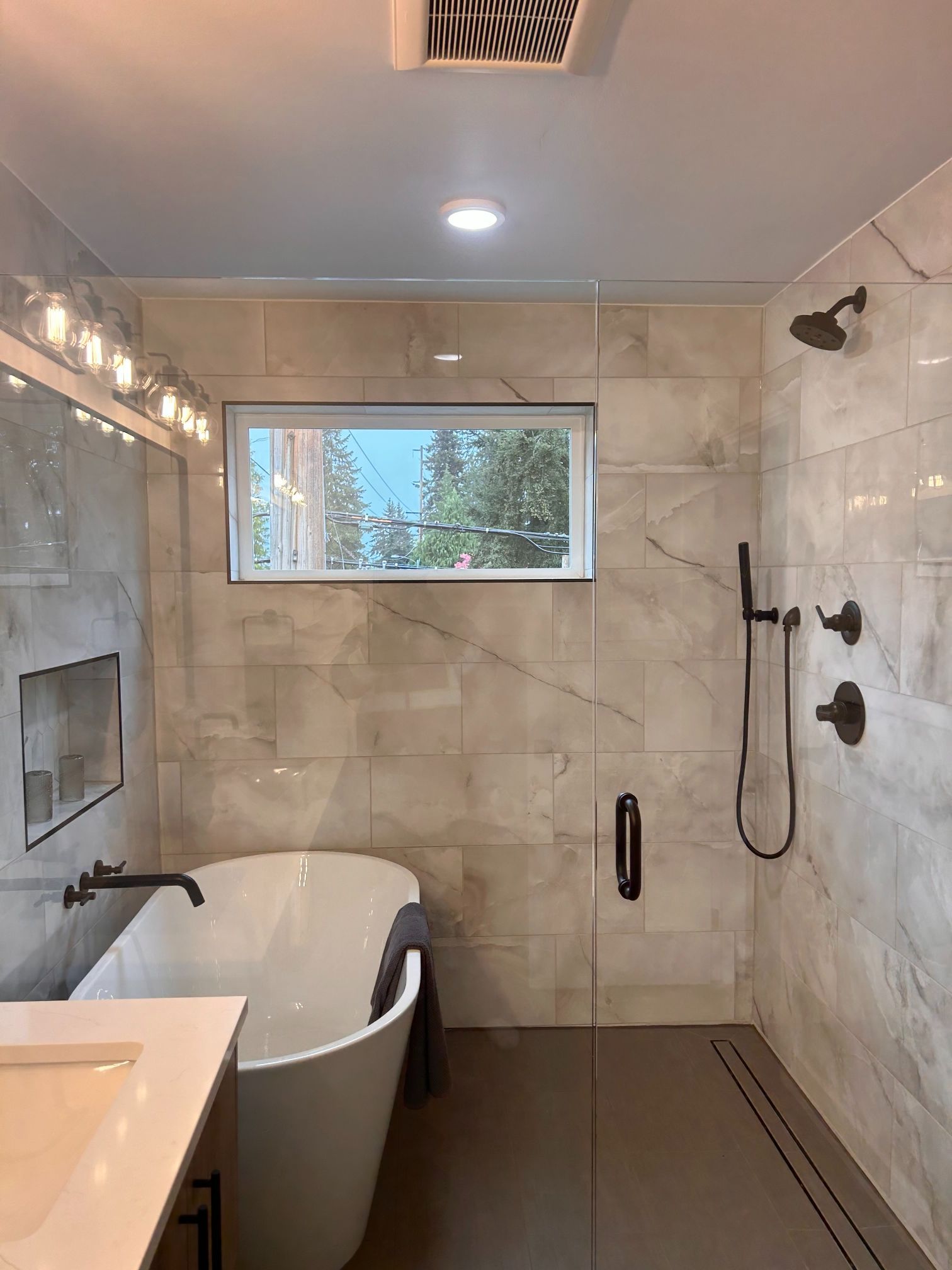 Modern bathroom with freestanding tub, walk-in shower, and frosted window overlooking trees