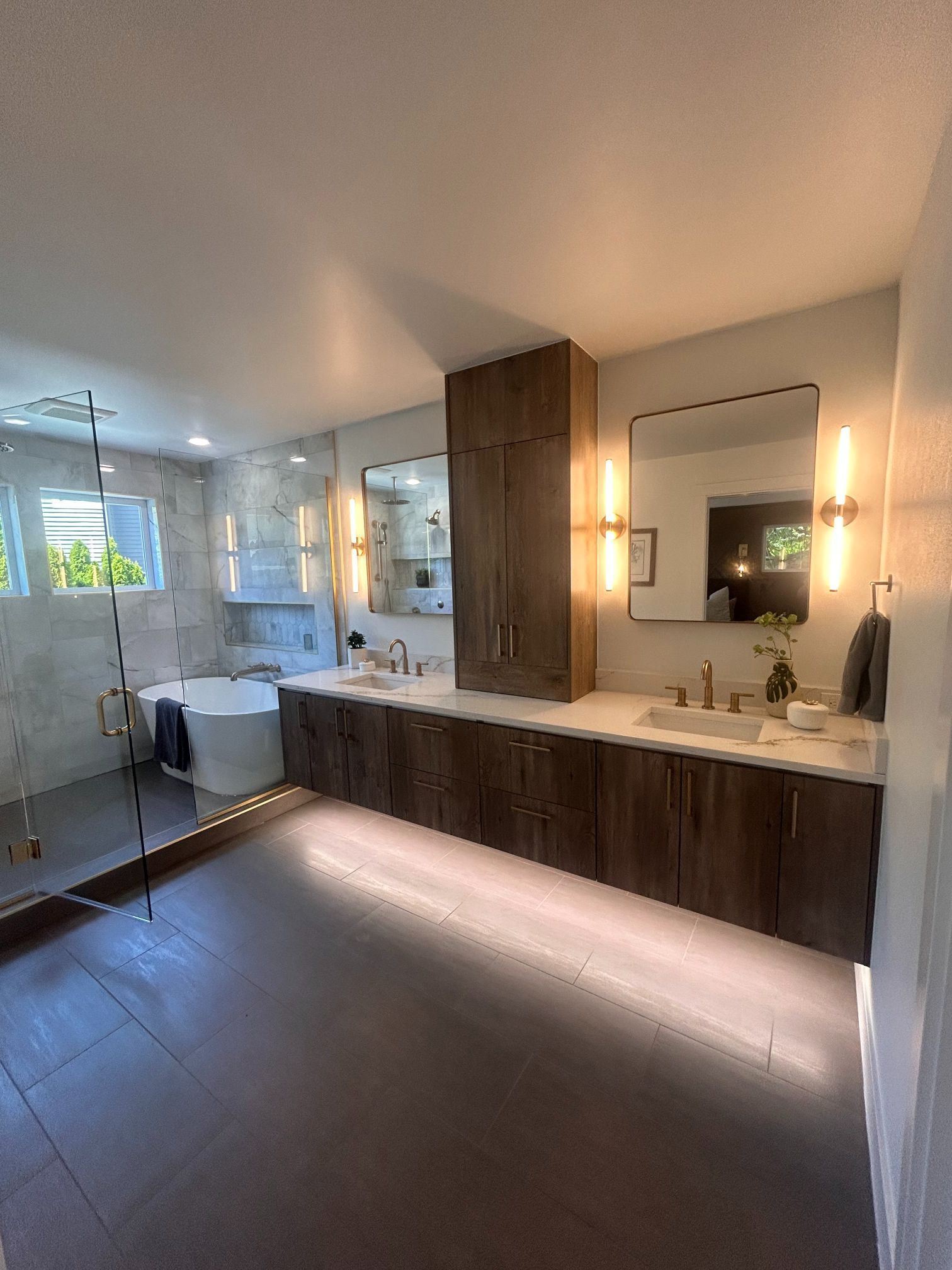 Modern bathroom with double vanity, wood cabinets, large mirror, and bright window lighting