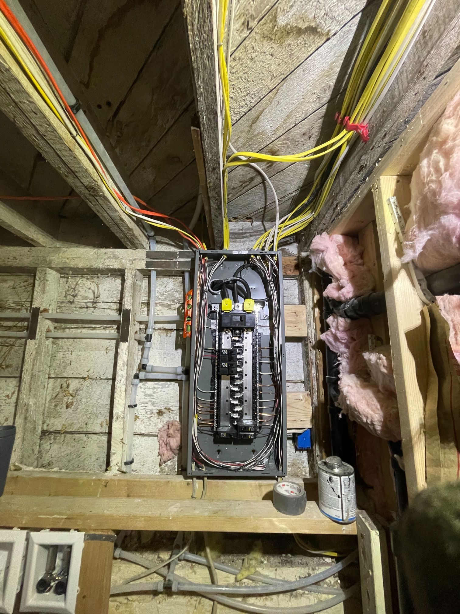 Open electrical breaker panel in an unfinished attic with exposed wiring and pink insulation