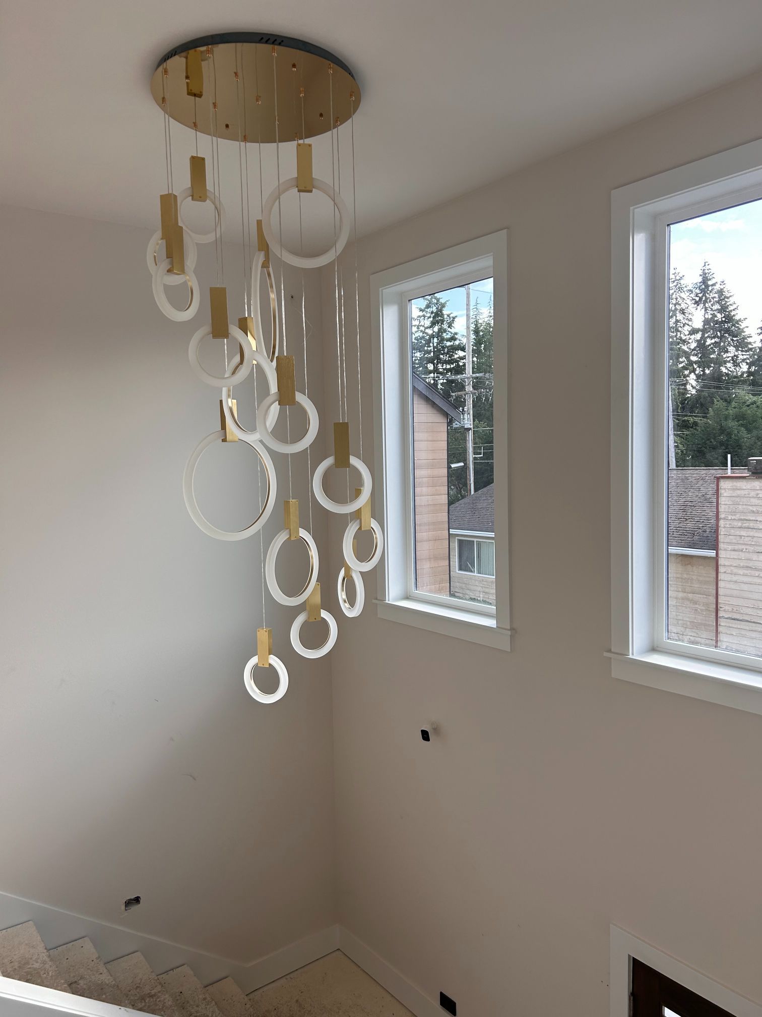 Modern ring chandelier hanging in a bright empty room with two windows and beige walls