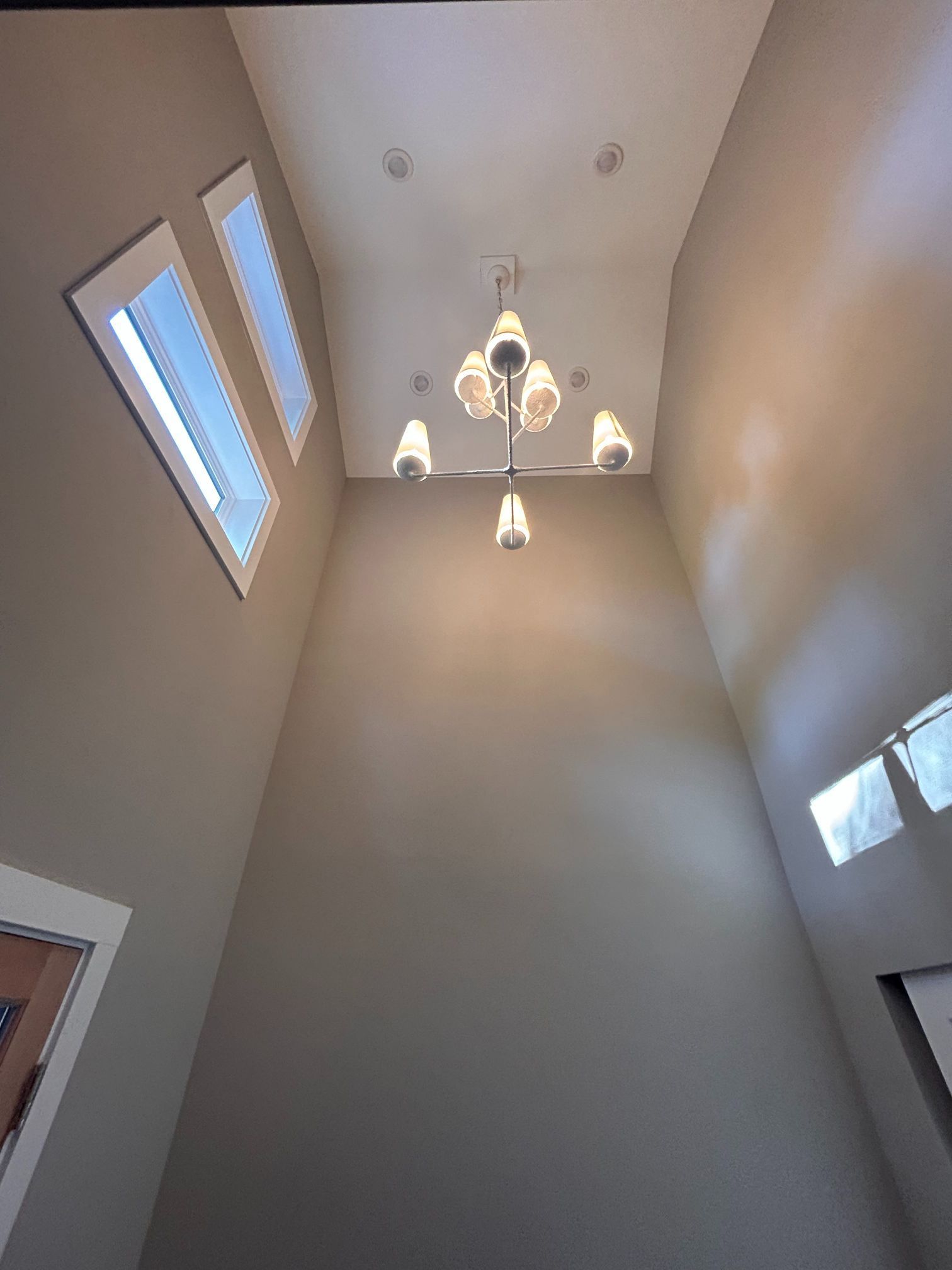 Tall beige foyer ceiling with chandelier and wall sconces, viewed upward from below.
